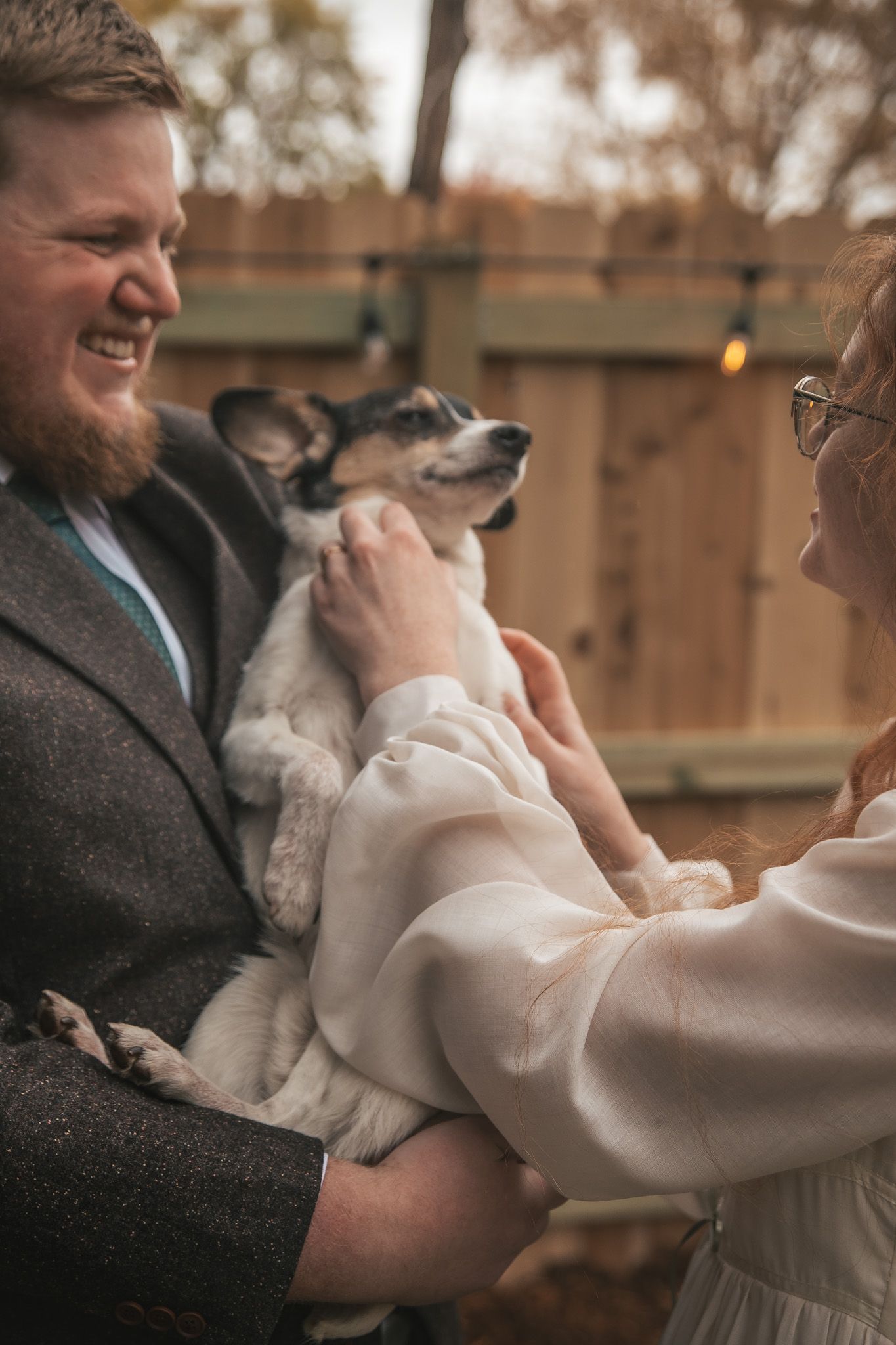 A small white dog is being lovingly held and cuddled in someone's arms while wearing a formal outfit.