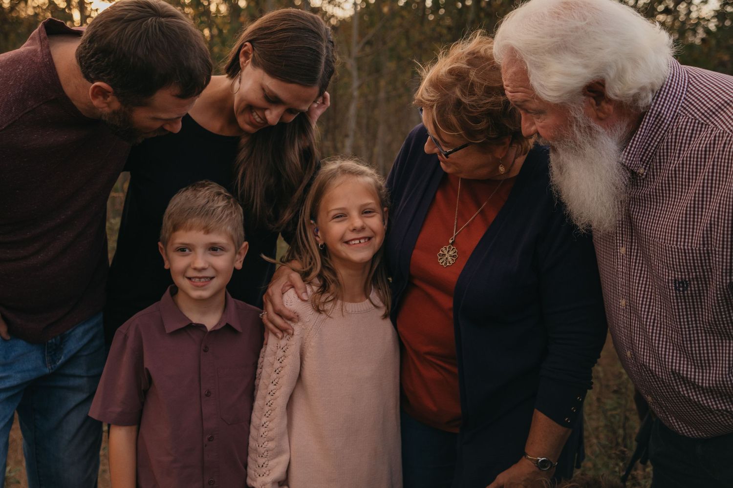 A group of people gather outdoors at sunset for a candid family photo session in casual attire.