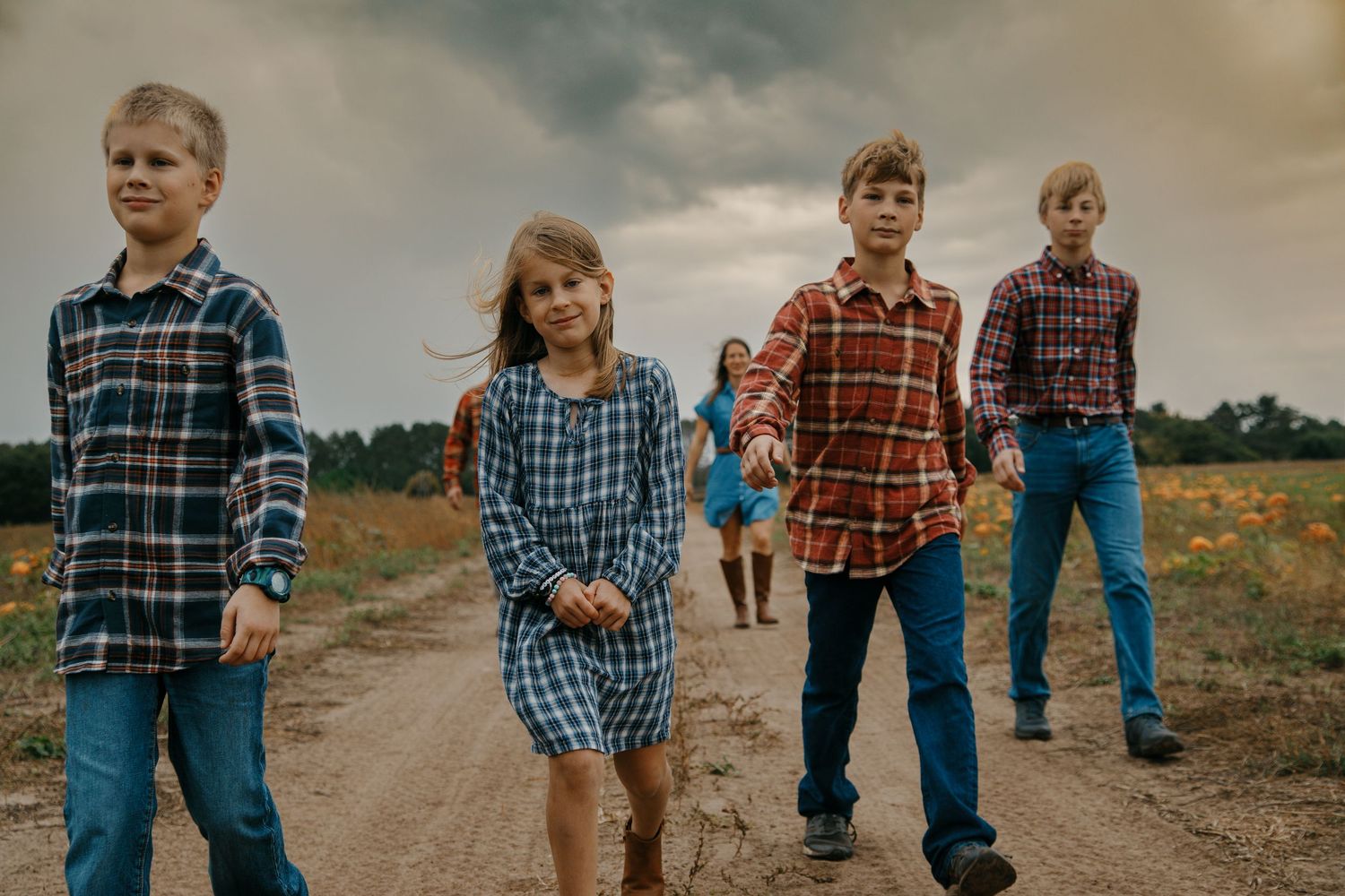 People walking together through a pumpkin patch on a cloudy autumn day with moody skies overhead.