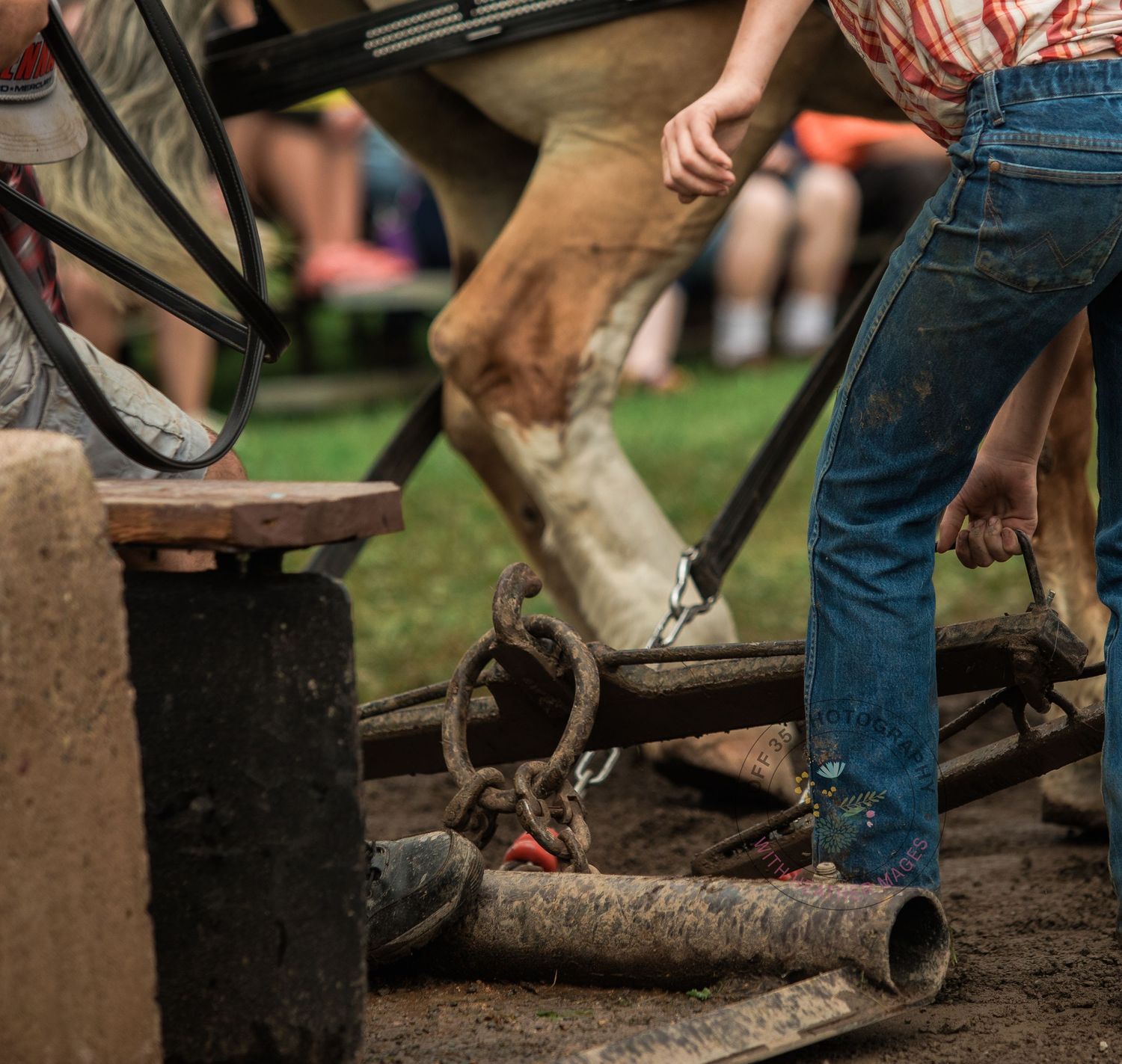 Close-up of work boots and jeans near industrial equipment on muddy ground.