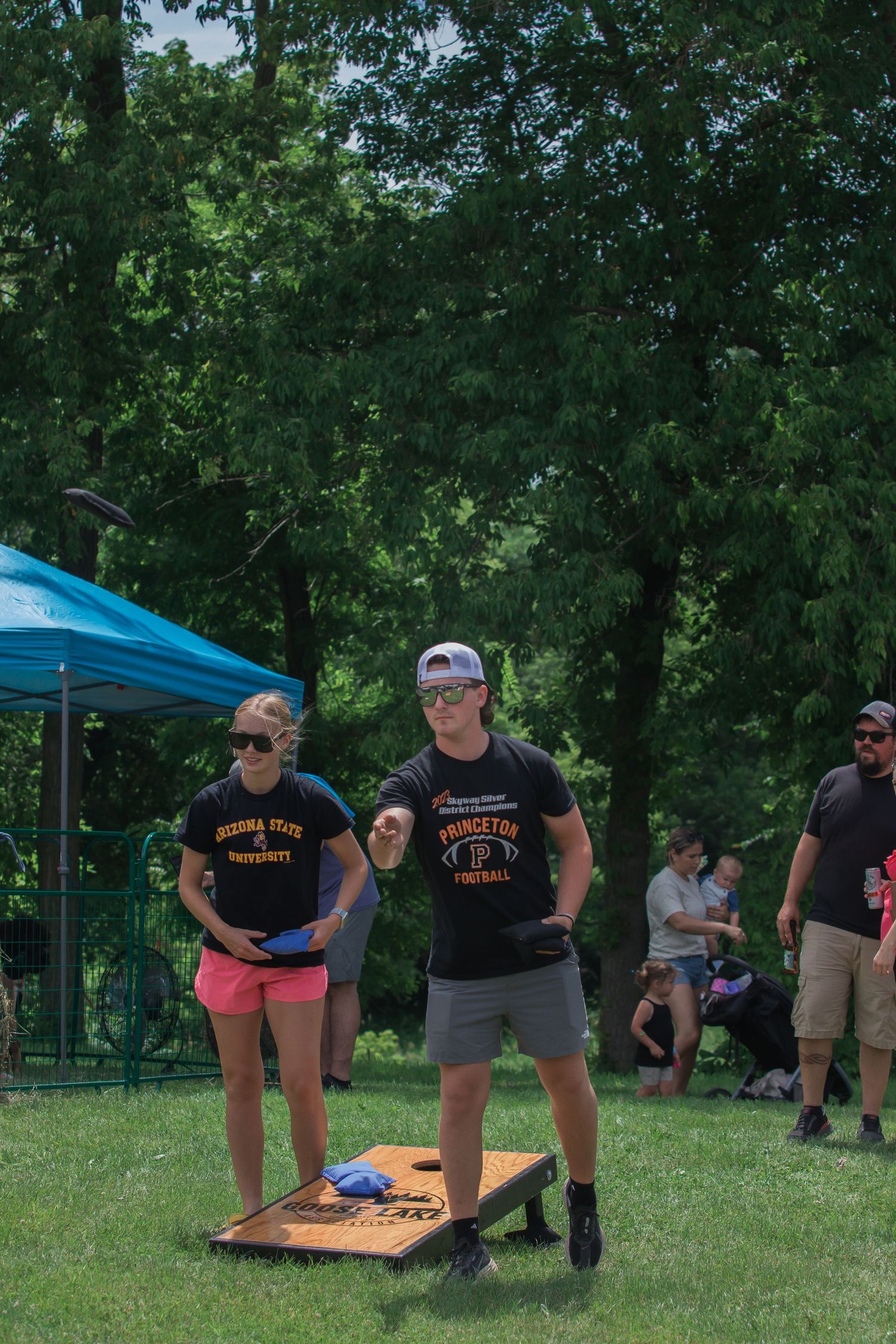 People in matching black t-shirts gather on a grassy field under trees during an outdoor event.