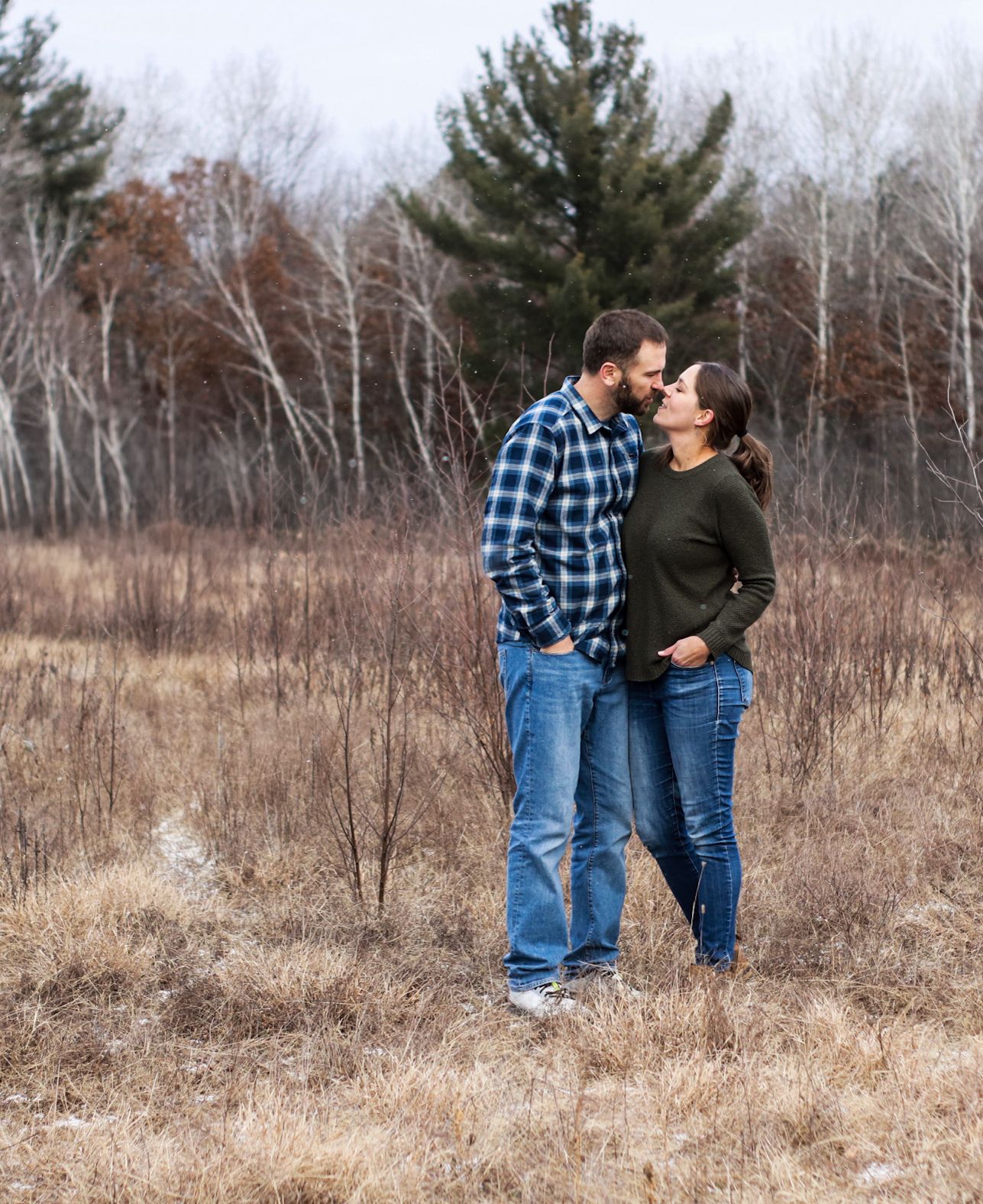 A couple shares an intimate moment in a field with birch trees in the background.