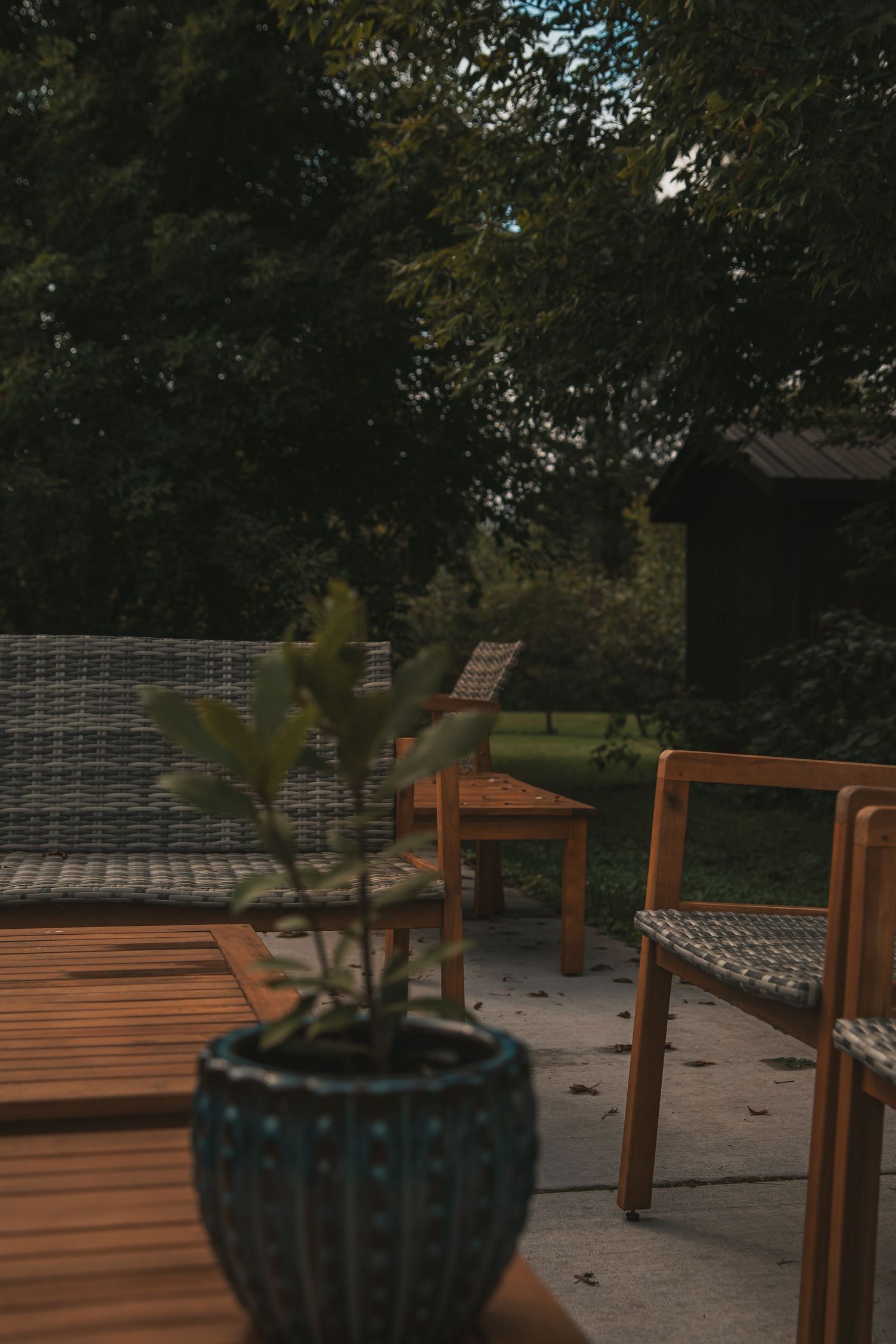 Wooden patio furniture with cushions and decorative planters arranged on an outdoor deck at dusk.