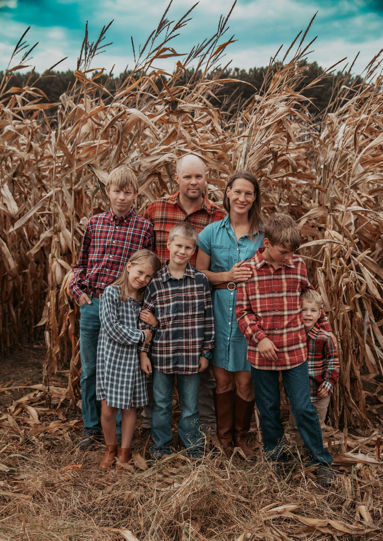 A group poses together in front of tall dried corn stalks on an autumn day.