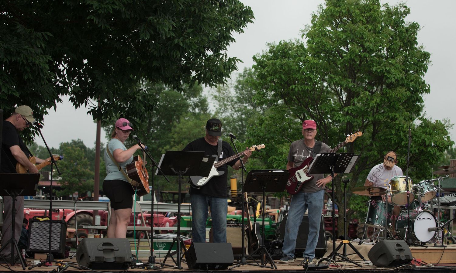 Band performing on outdoor stage with guitars and drums during a summer festival.