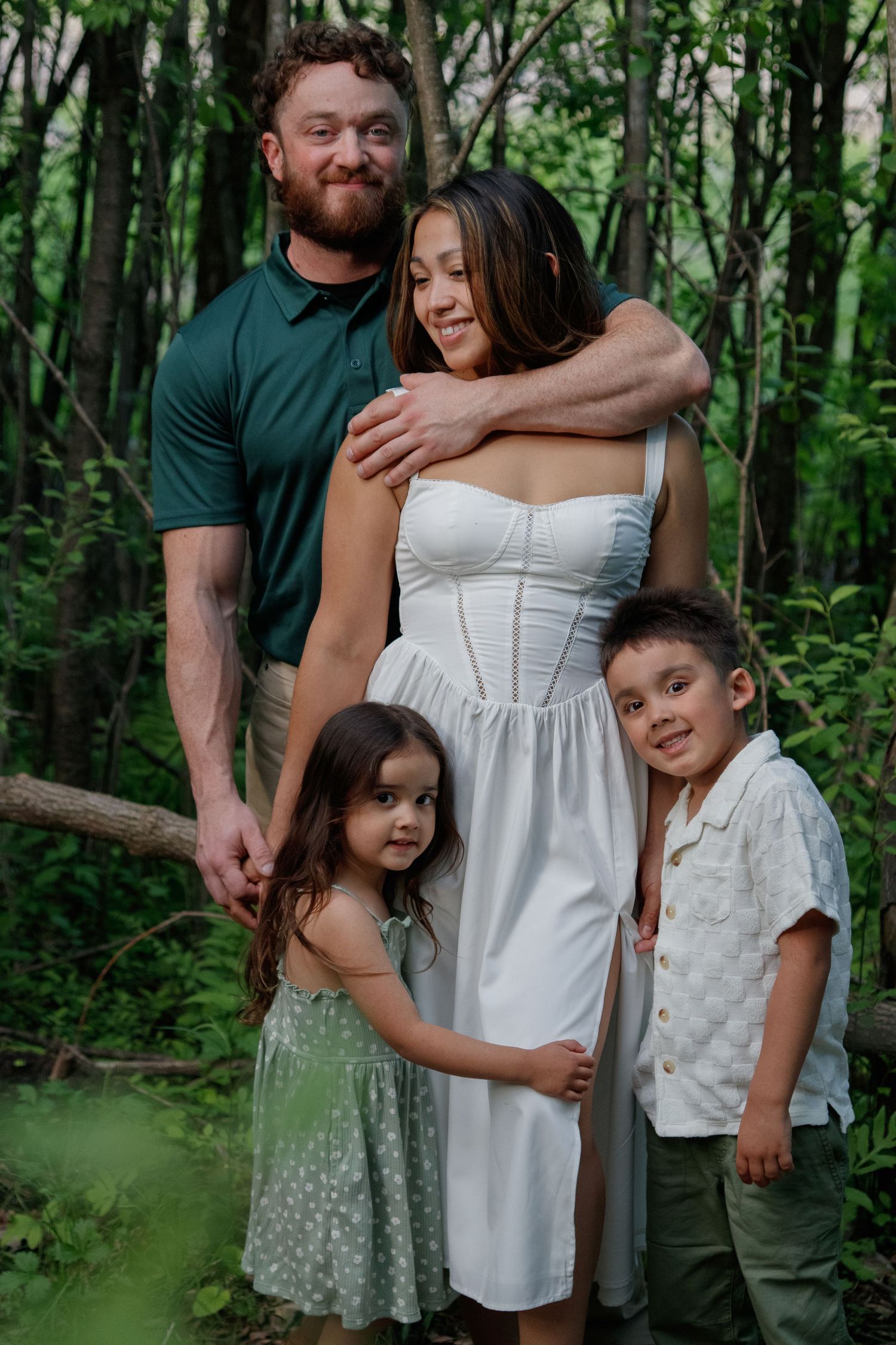 A family poses together for a portrait in a lush green forest setting wearing coordinated outfits.
