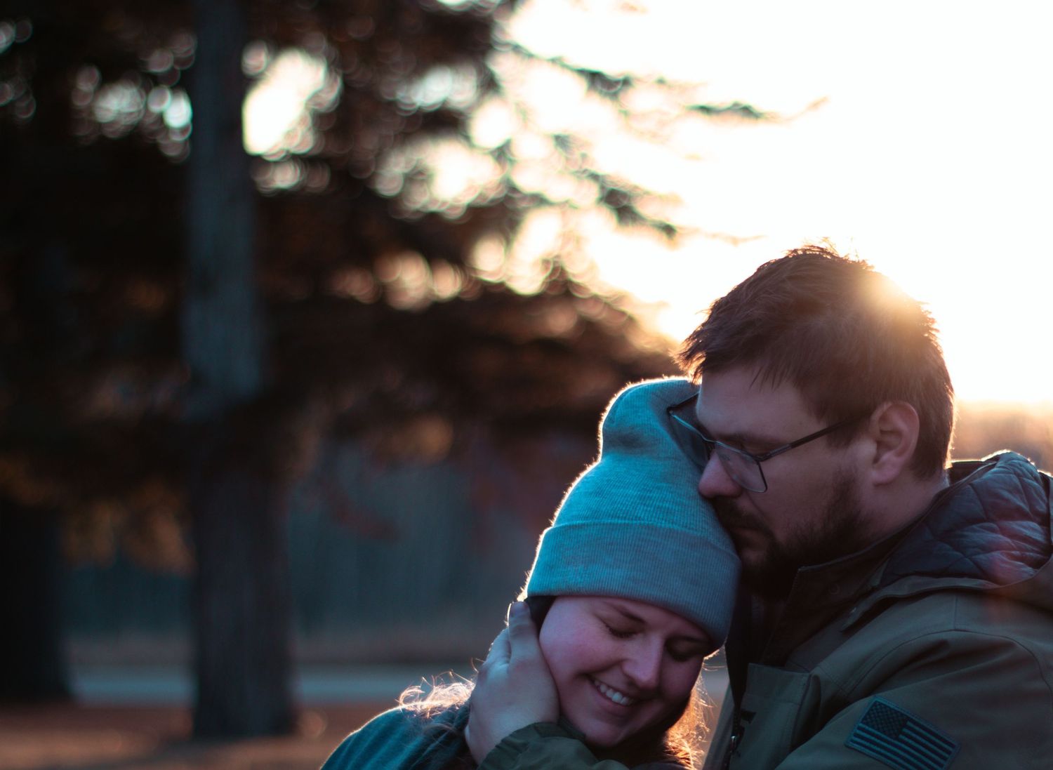 A couple shares an intimate moment at sunset while wearing cozy winter clothing.