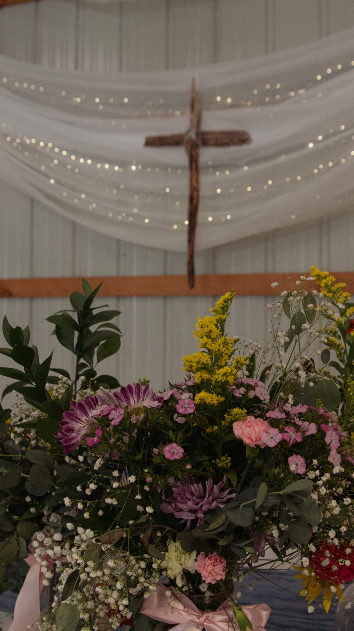 Wedding reception venue decorated with draped white fabric, twinkling lights, and colorful floral arrangements on display.