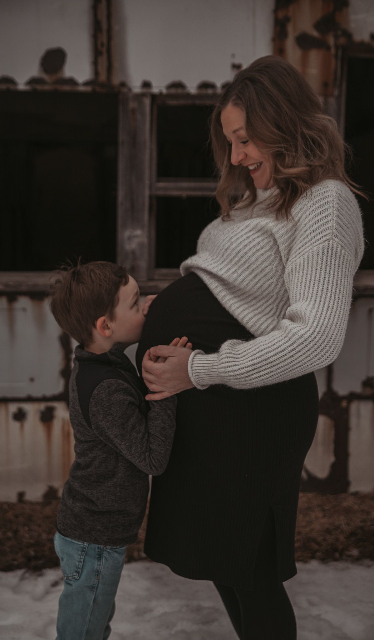 Family maternity photo shoot with young child touching pregnant belly in winter setting.
