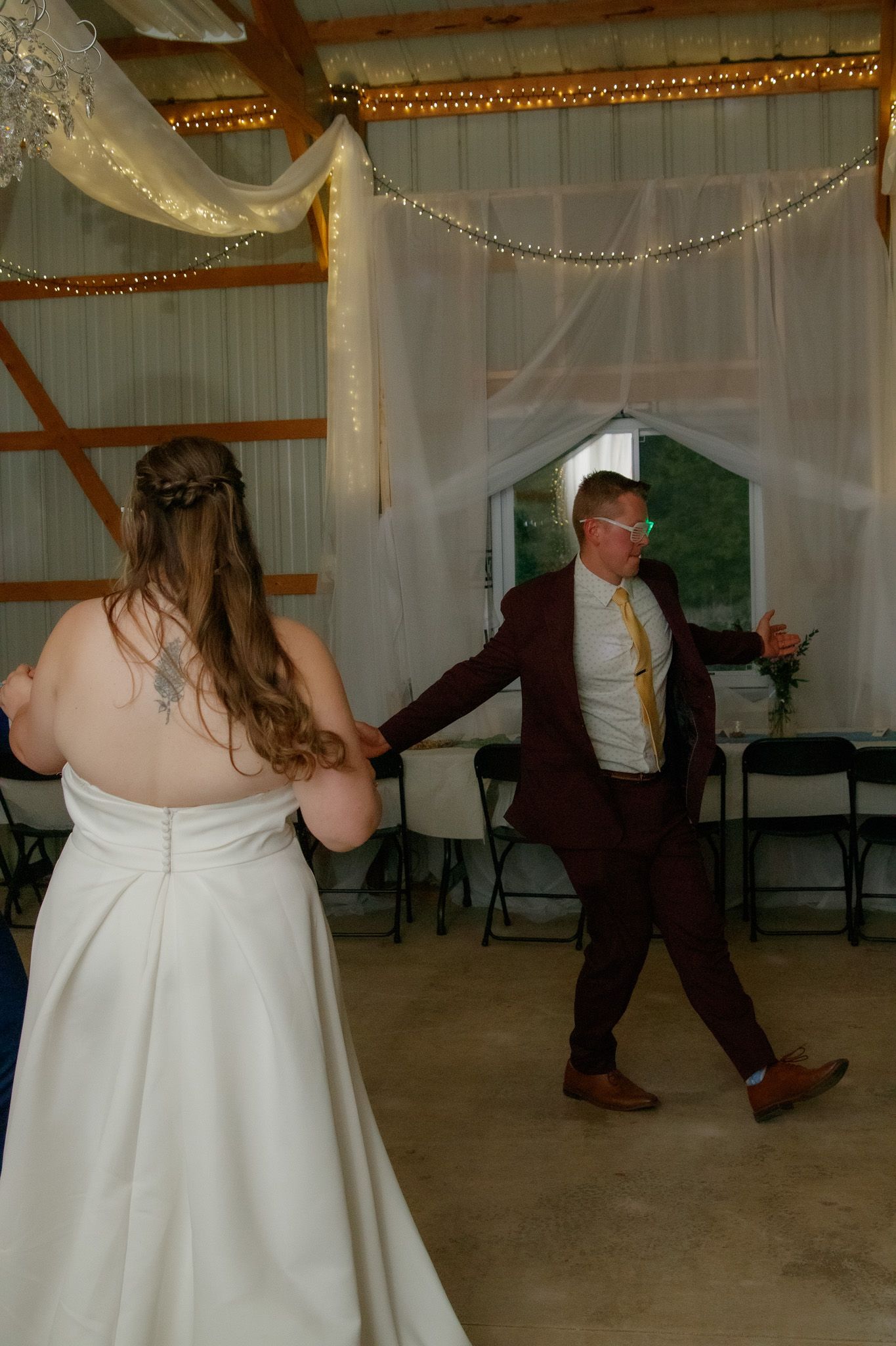 People dancing at a rustic barn wedding reception with white tulle decorations and string lights overhead.