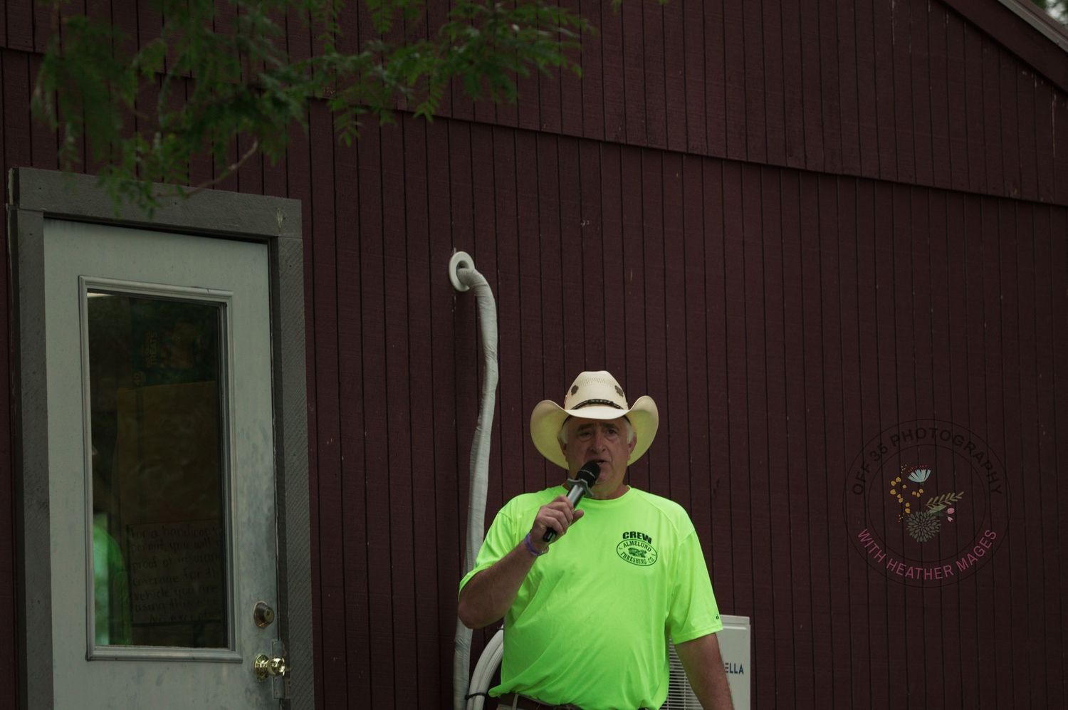 Someone in a bright green shirt and cowboy hat stands in front of a brown building with a white door.