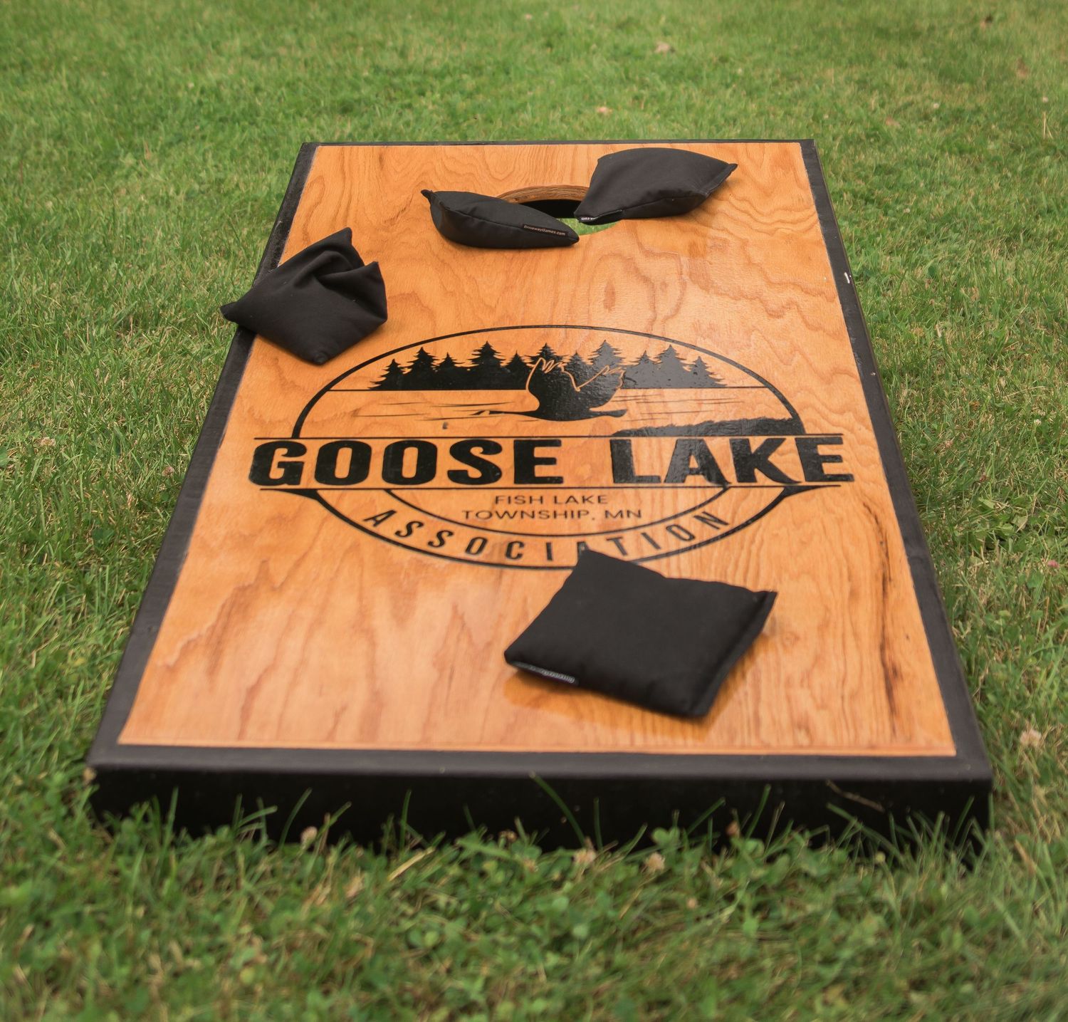 Custom wooden cornhole board with Goose Lake logo design shown from multiple angles on grass.
