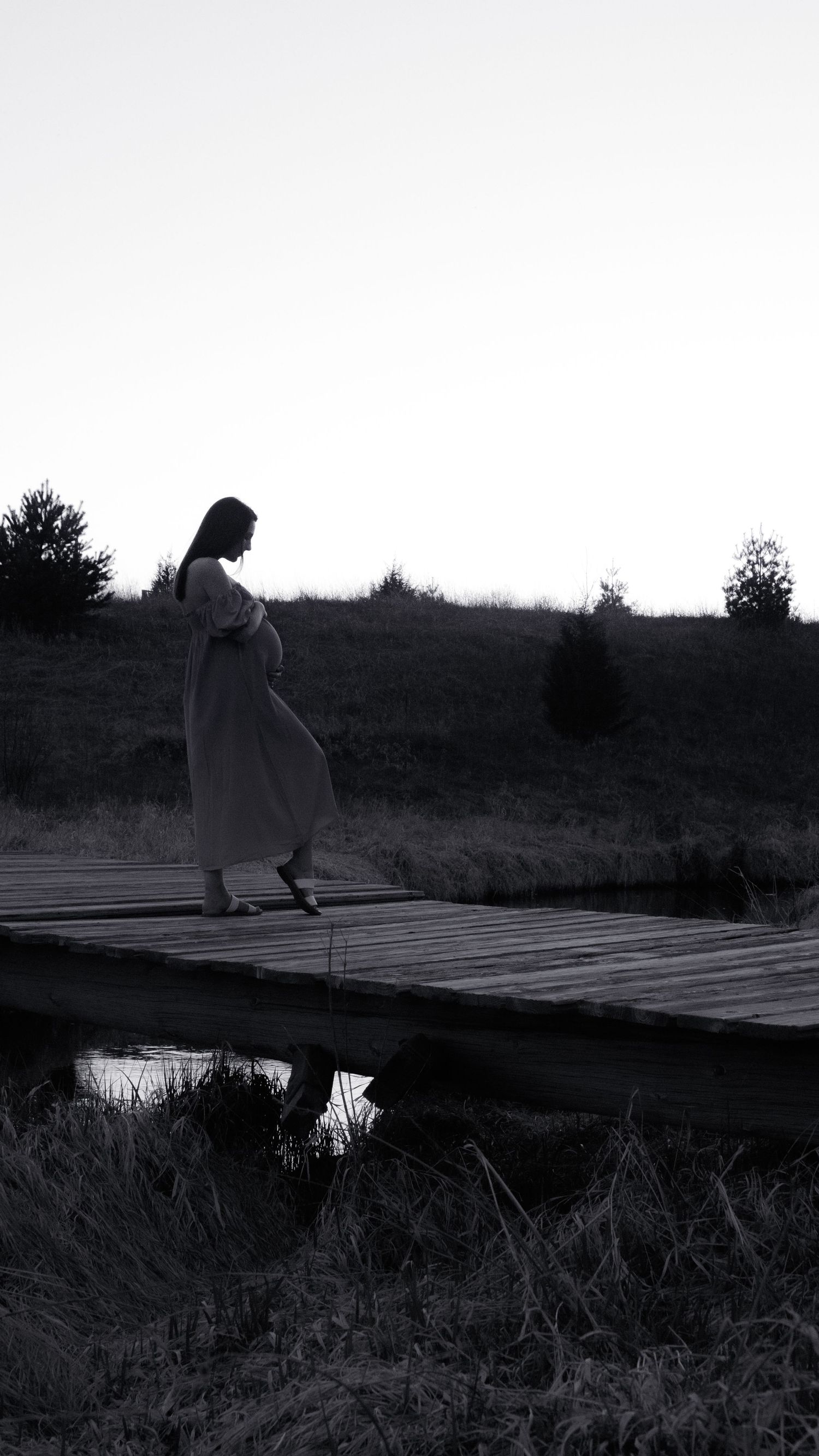A silhouetted figure walks along a wooden boardwalk at dusk creating a moody atmospheric scene.