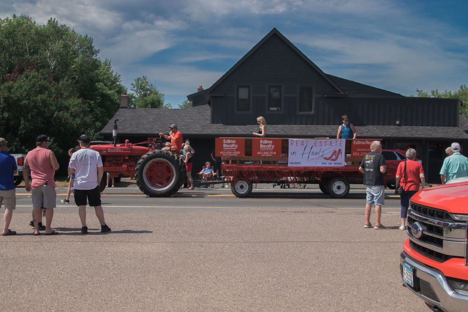 A vintage red tractor and wagon on display at an outdoor event near a black barn building.