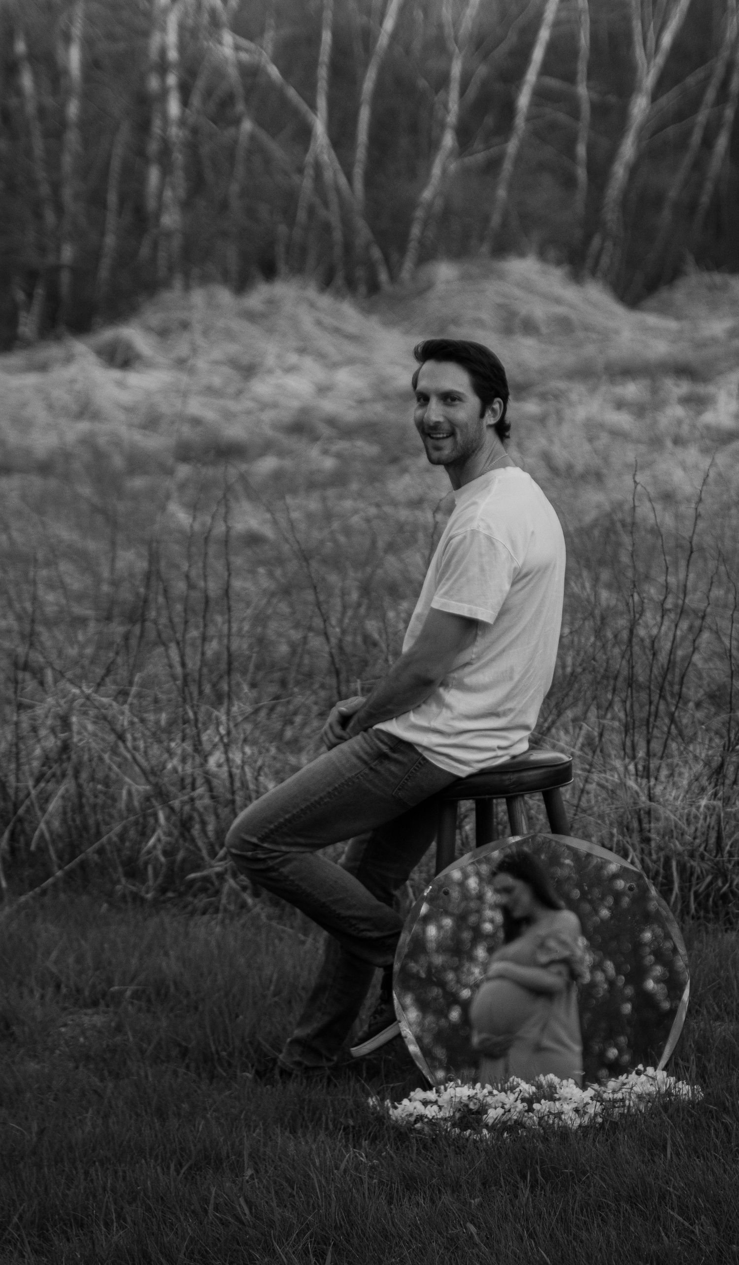 A person in a white t-shirt sits outdoors in a field of wildflowers at dusk, captured in black and white photography.