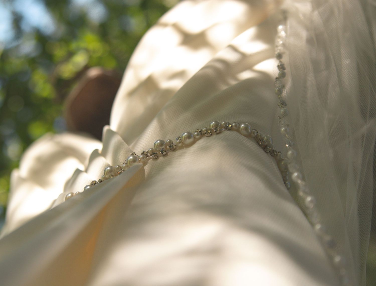 Close-up view of a delicate white wedding dress with intricate lace and beaded details in natural lighting.