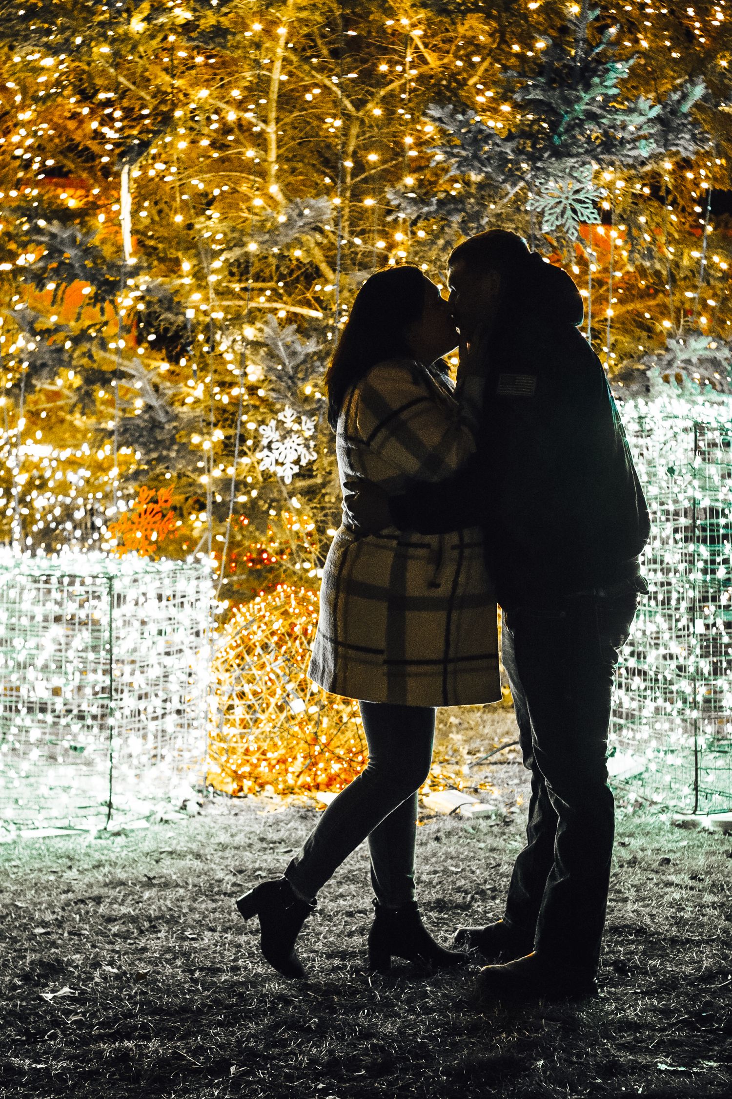 Two silhouettes stand together against a backdrop of glowing golden autumn leaves creating a romantic scene.