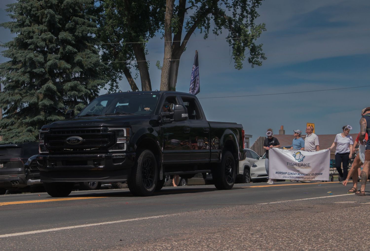 A line of black pickup trucks parked along a shoreline with people gathered nearby.