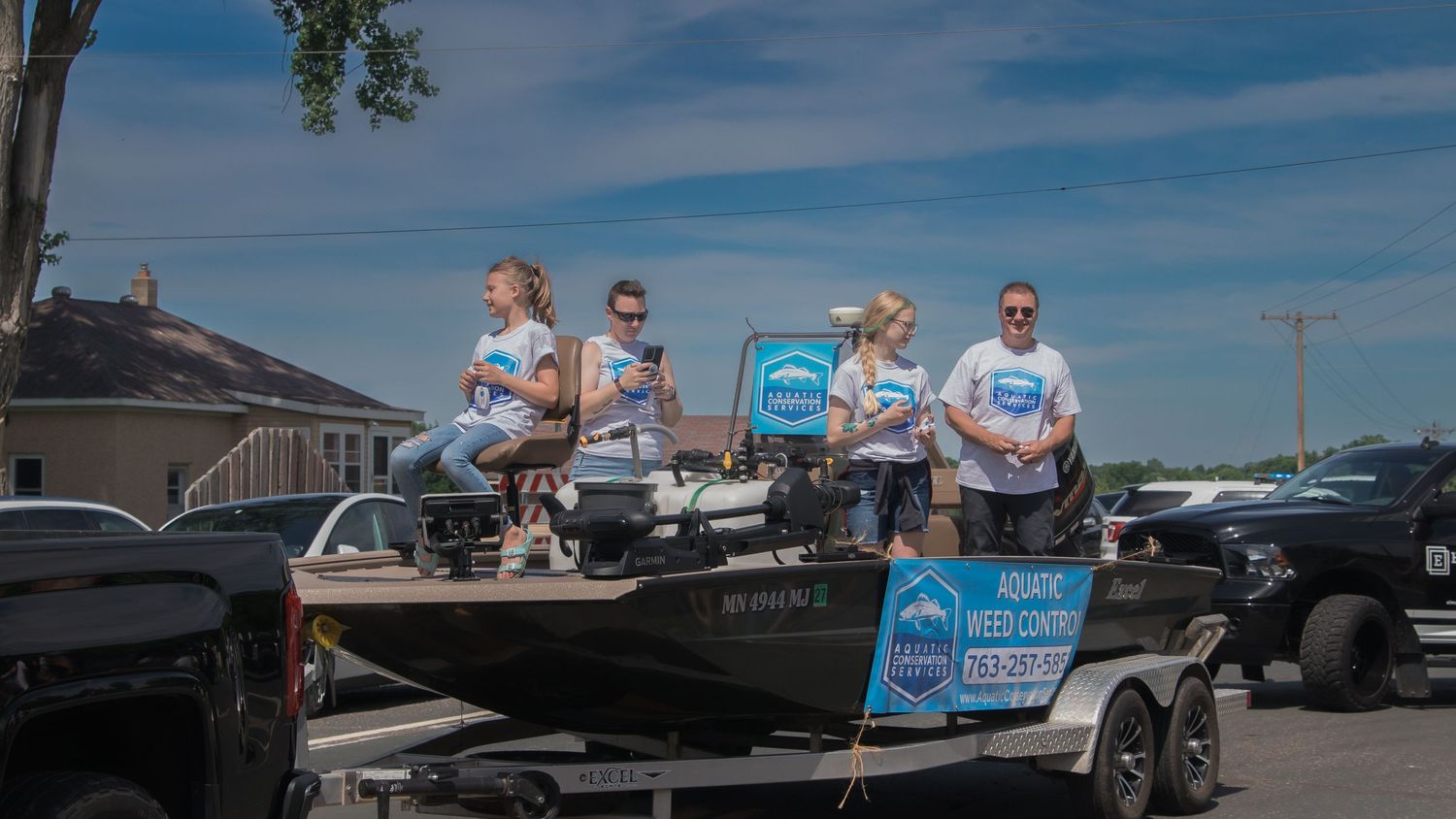 People seated on a boat trailer decorated with banners at an outdoor event.