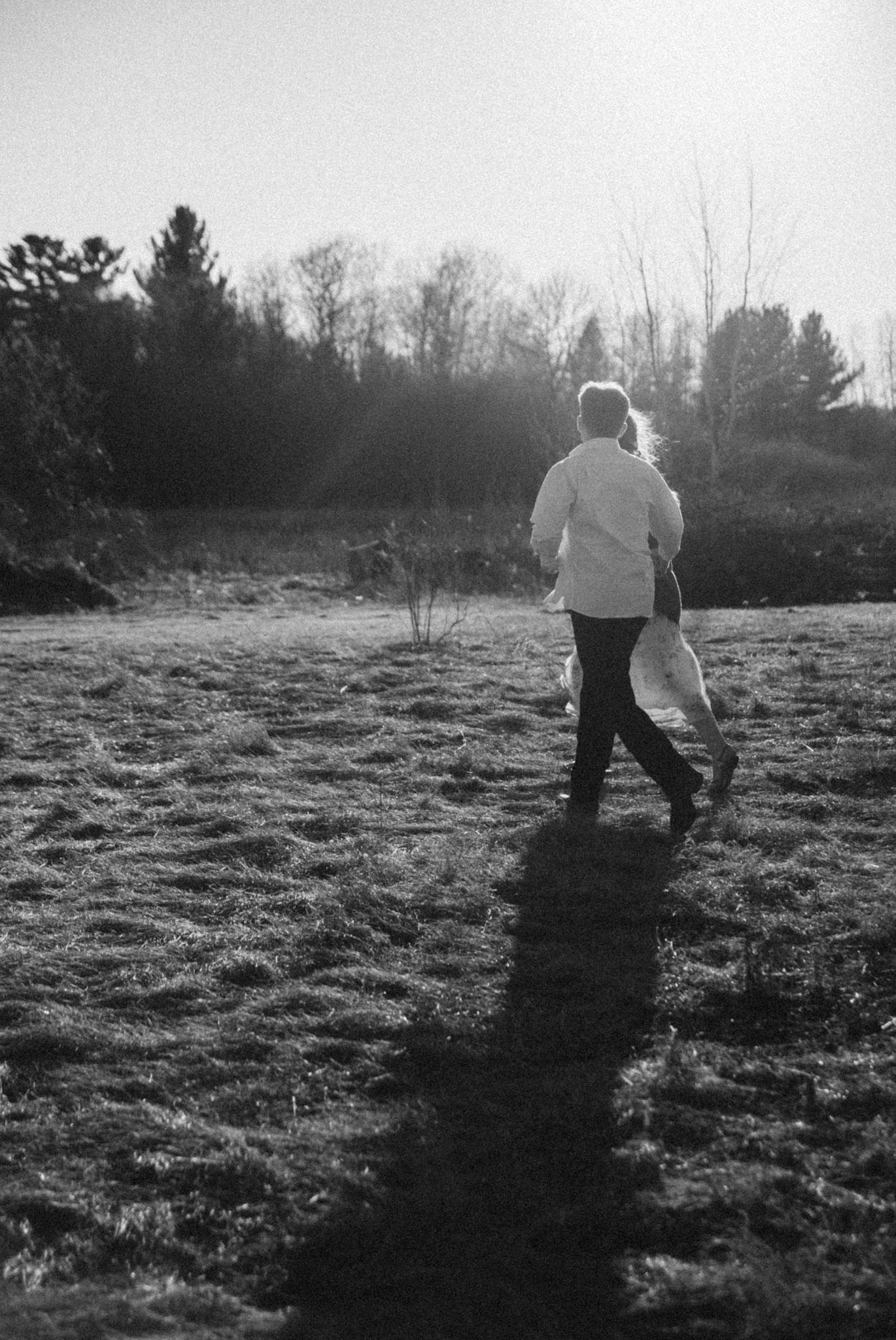 A person walks alone across a frost-covered field at sunrise in a dreamy black and white photo.