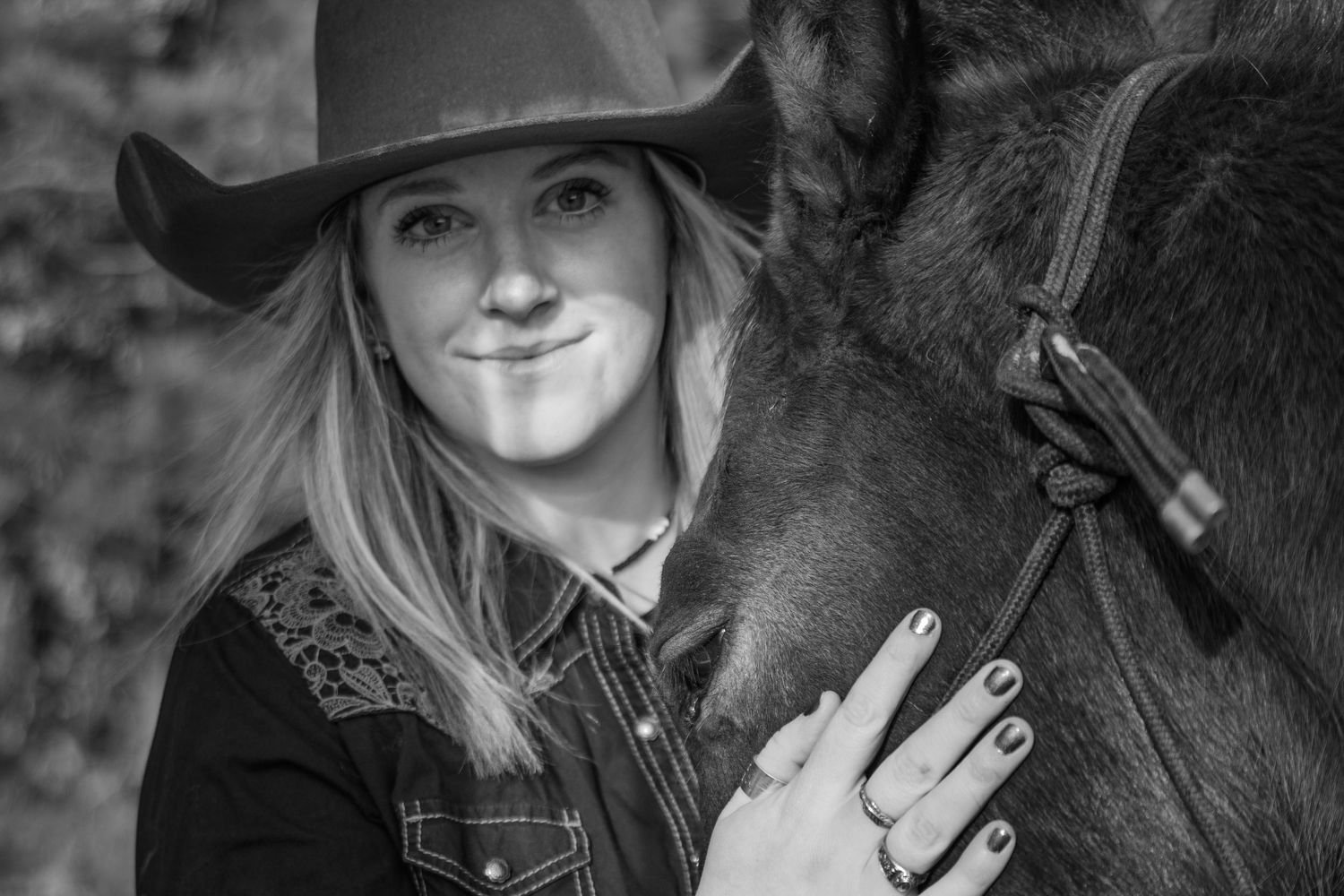 A black and white photo shows a close interaction between someone wearing a cowboy hat and their horse.