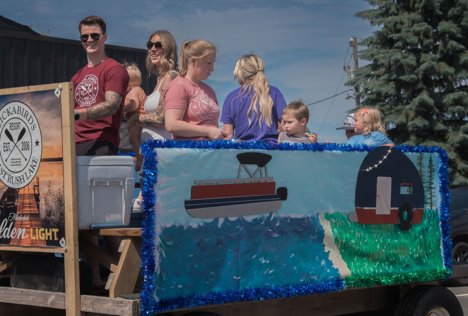 A group rides on a float decorated with blue and green ocean-themed artwork in a parade.