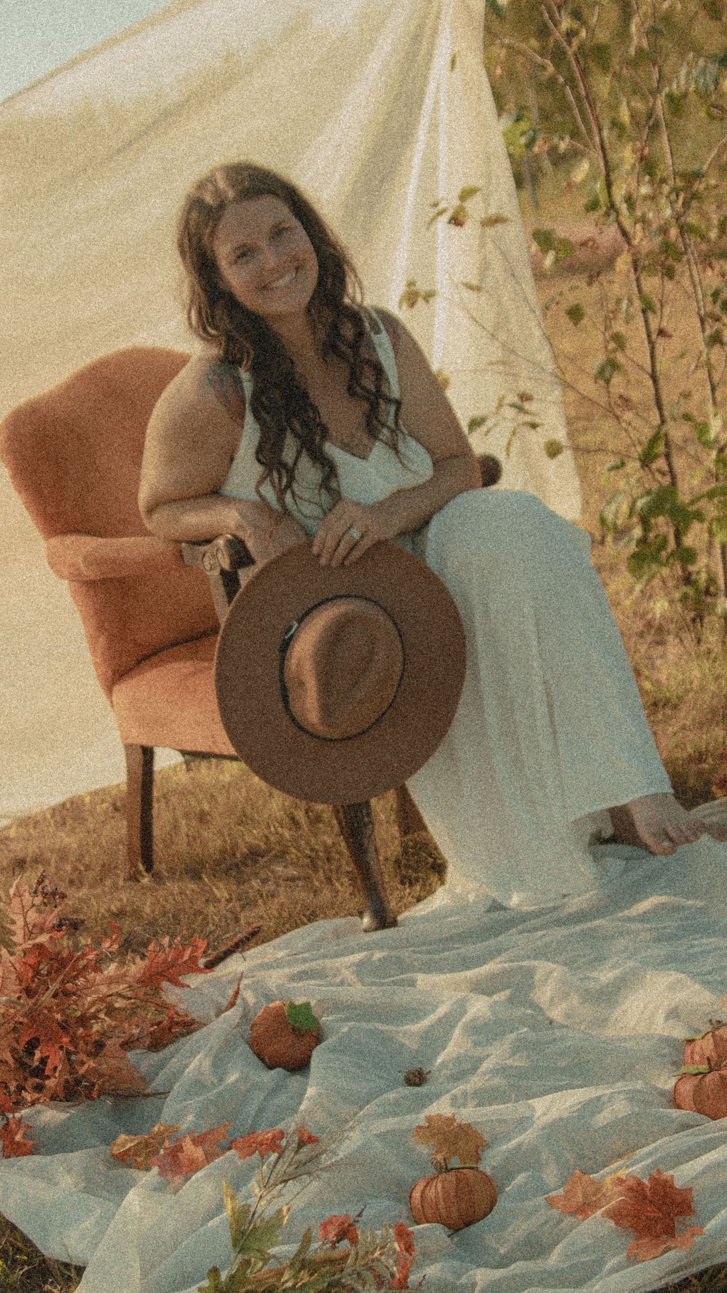 Autumn outdoor portrait session with fall foliage, pumpkins, and a vintage brown armchair on a blue blanket setting.