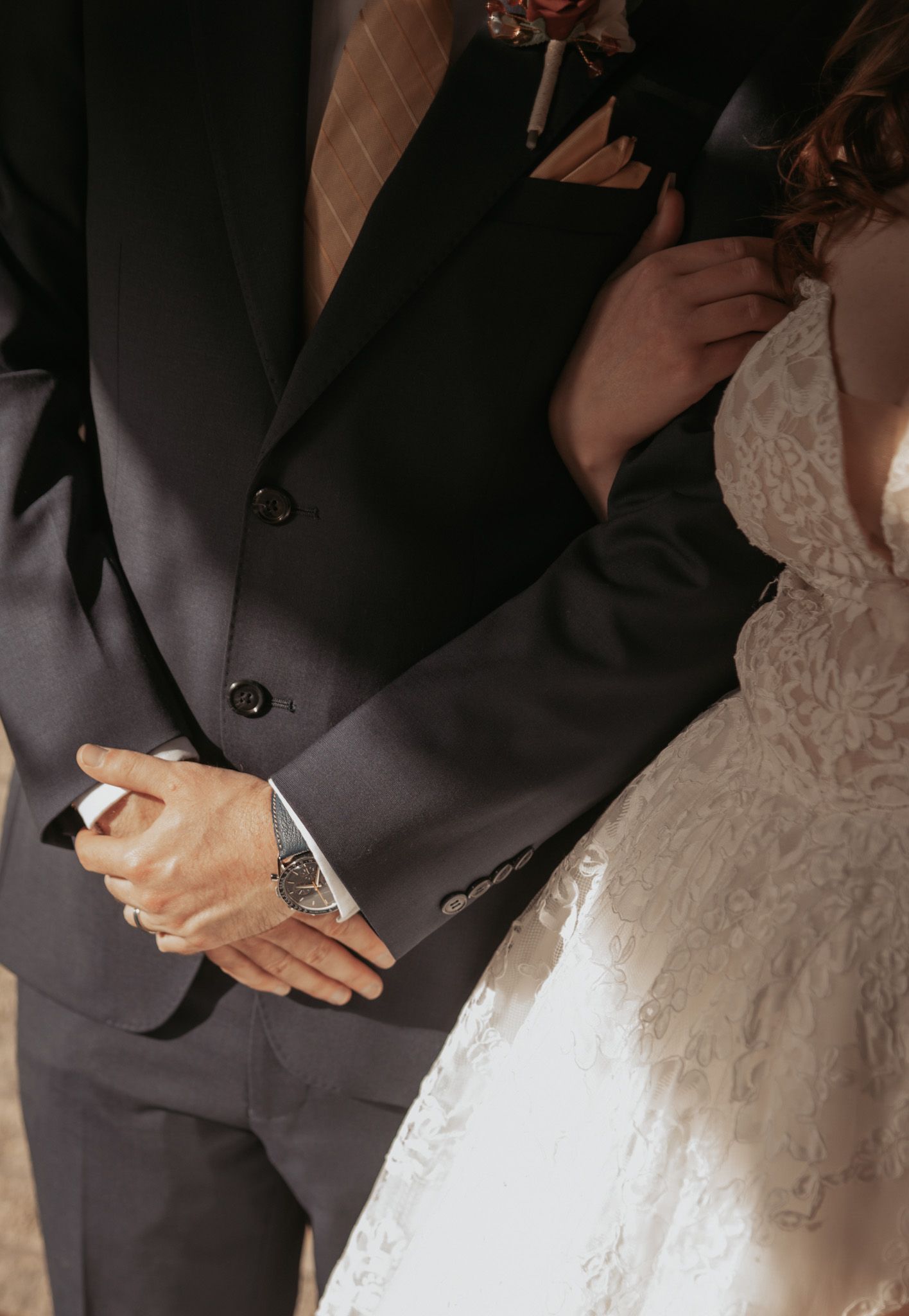 Close-up detail of a couple's hands during their wedding ceremony, with formal attire and white lace dress visible.