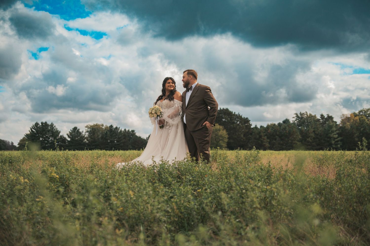 A couple shares a romantic moment in a golden field under dramatic cloudy skies during a wedding photo session.