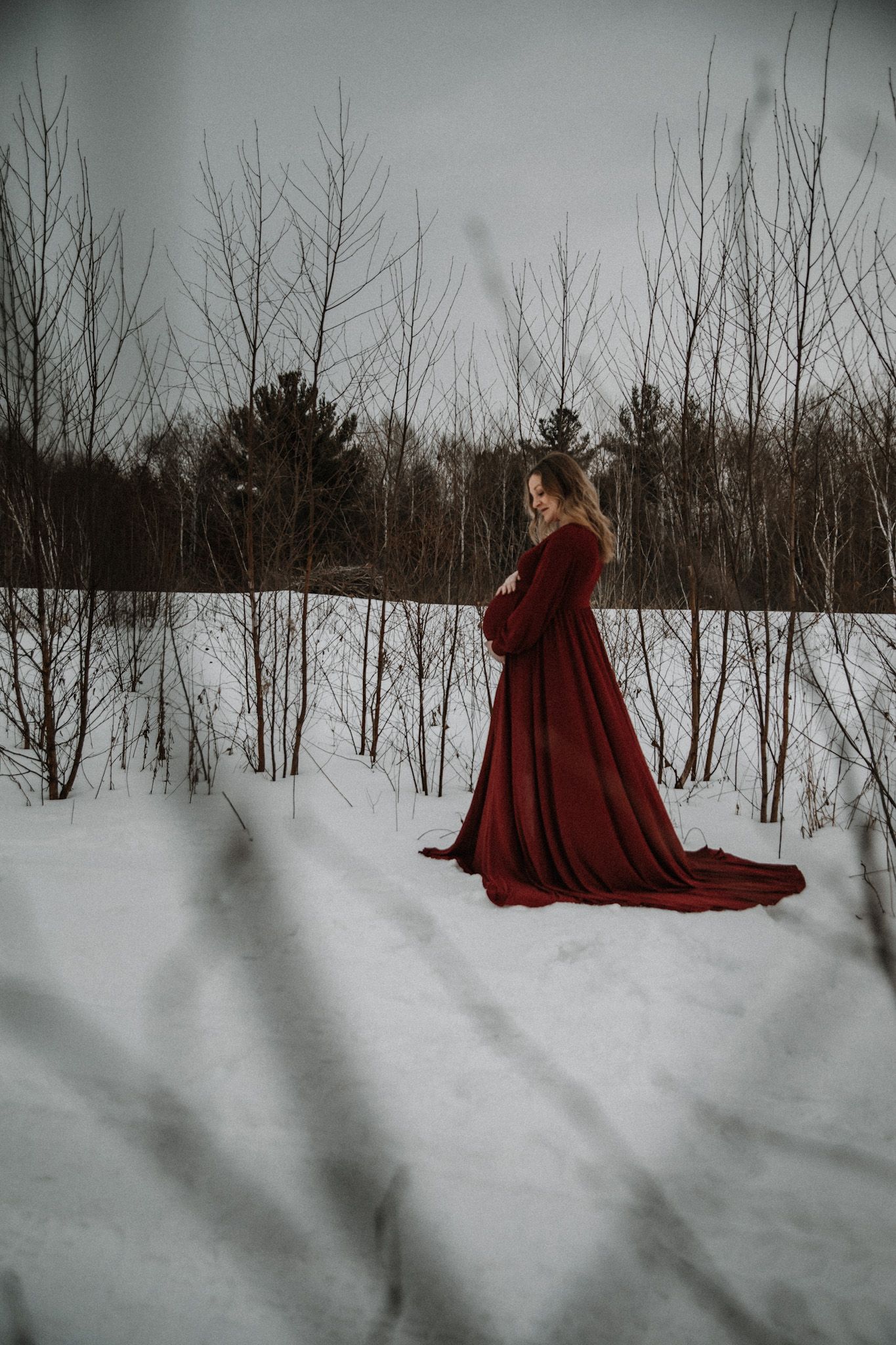 A figure in a flowing red cloak walks through a snowy winter forest landscape creating a dramatic contrast.