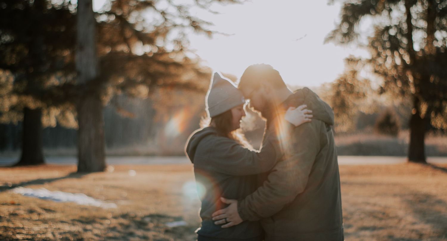 A romantic silhouette embraces in a park during golden hour as sunlight glows through autumn trees in the background.