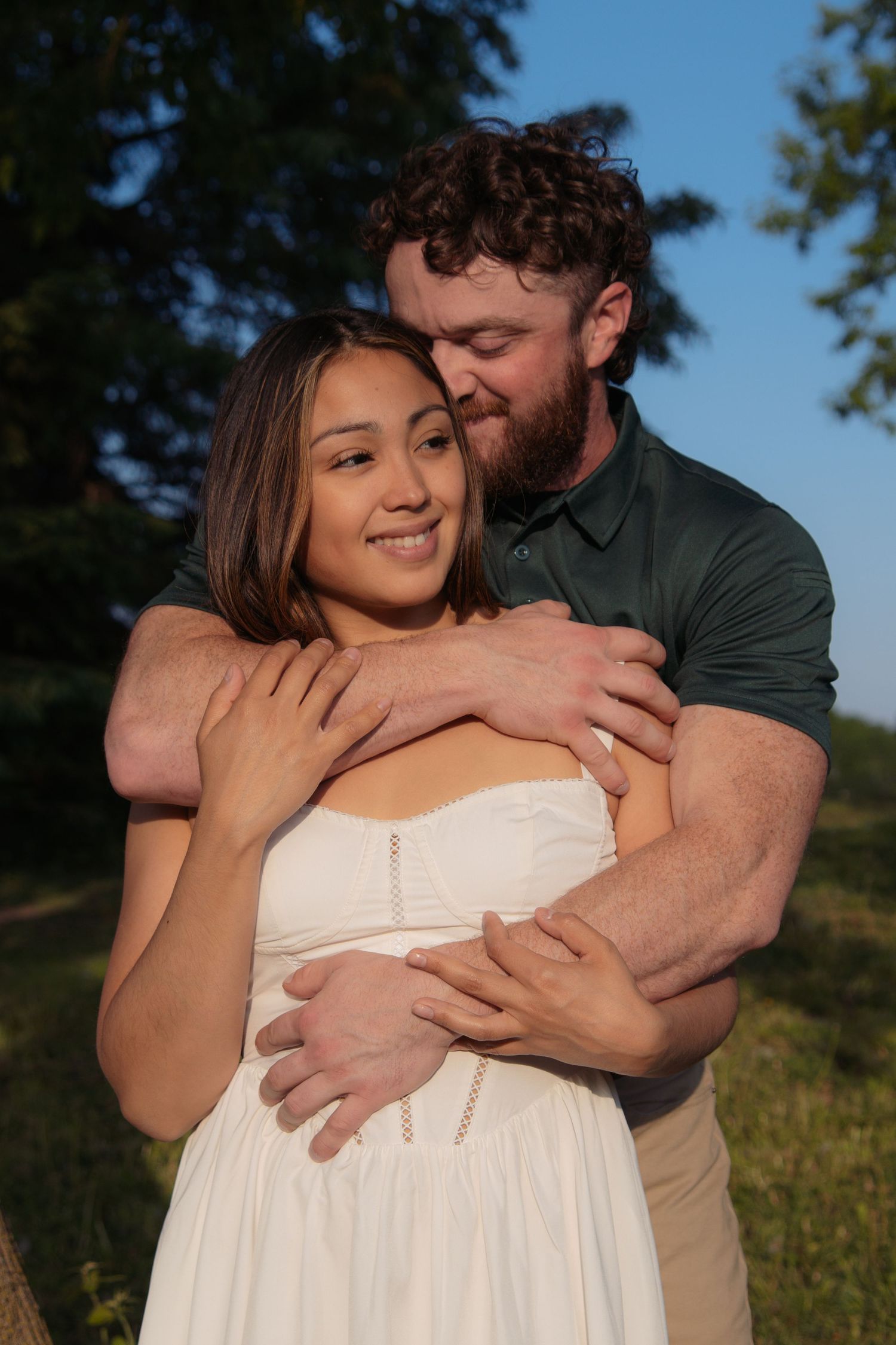 A romantic couple embraces in an outdoor setting during golden hour with greenery in the background.