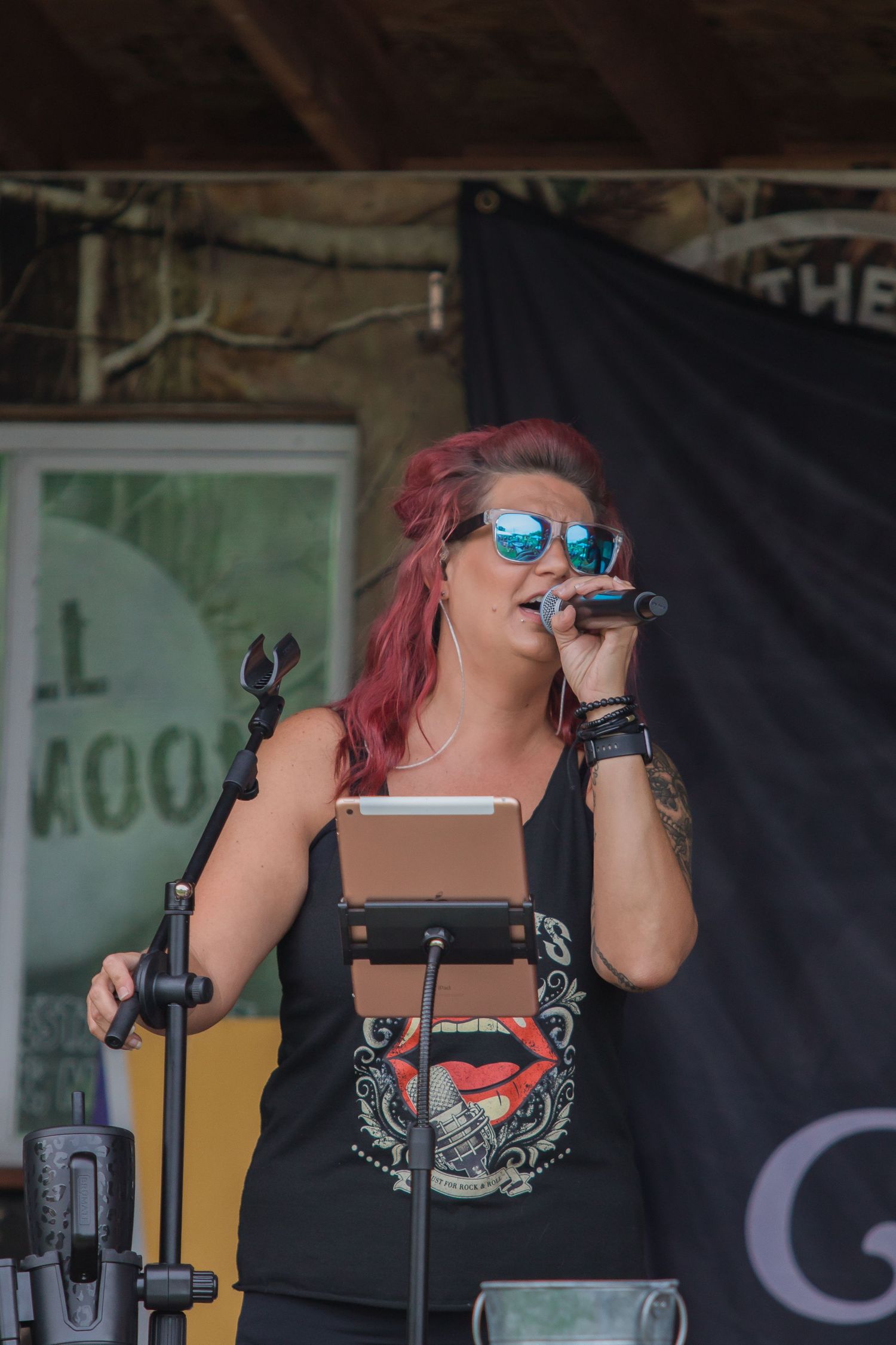 Singer performing on stage with microphone against black backdrop and venue signage.