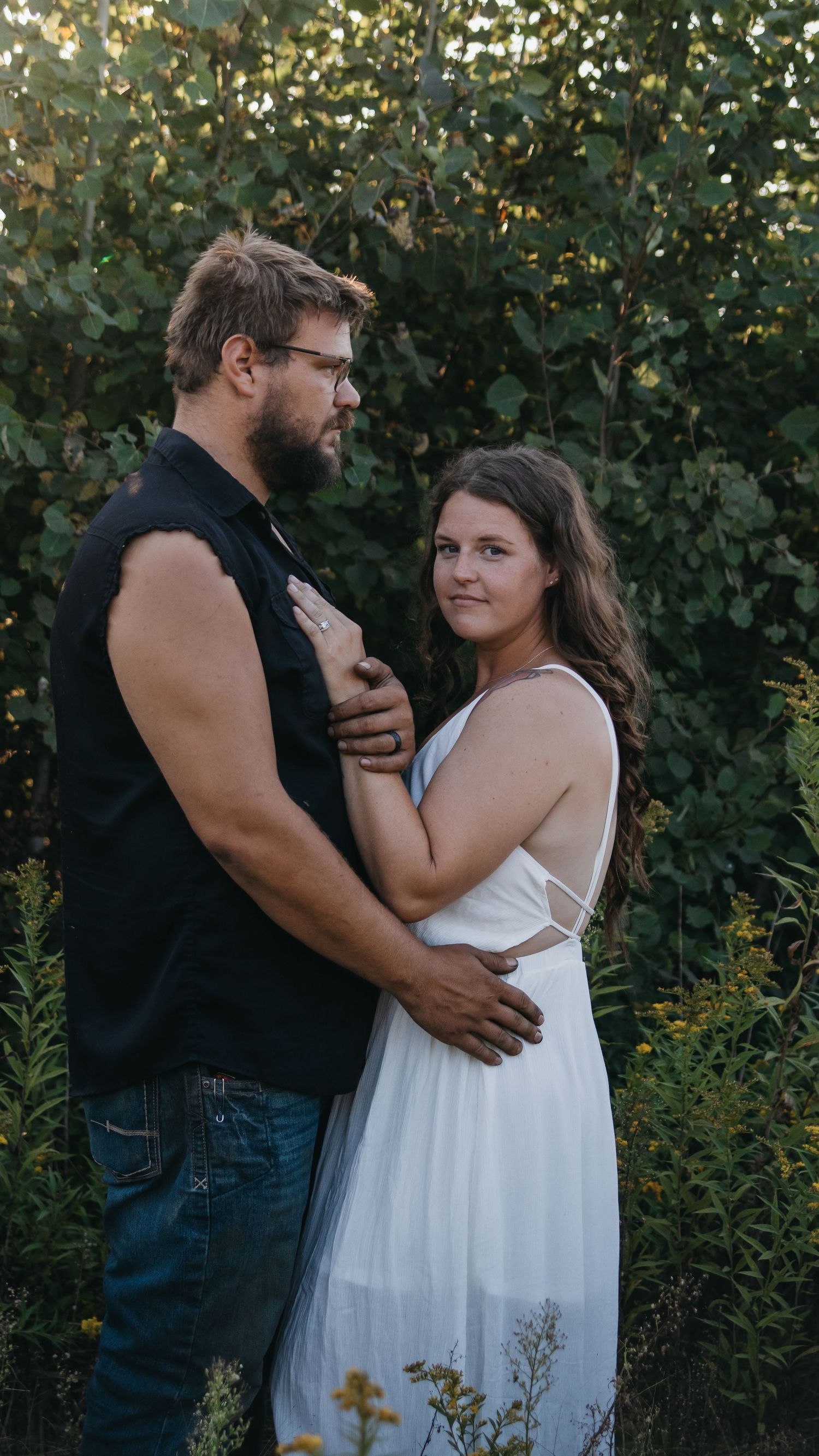 Couple embraces intimately in an outdoor garden setting, with green foliage in the background.