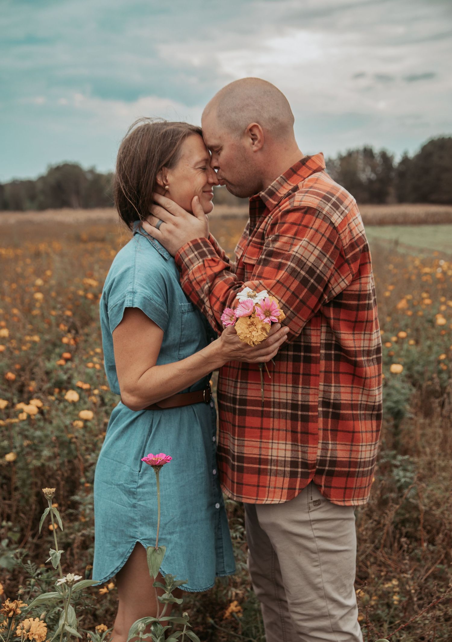 Romantic couple sharing an intimate moment in a wildflower field during autumn, with her in blue dress and him in plaid.
