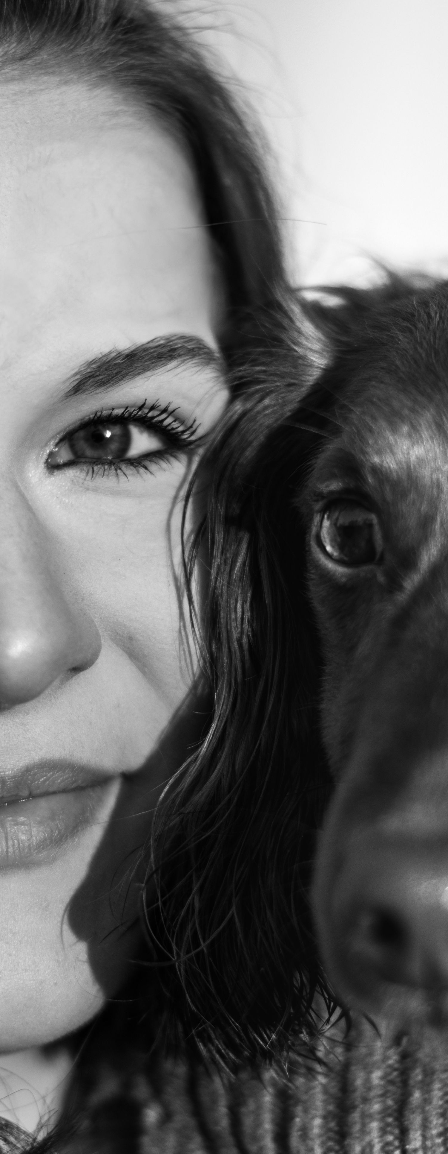 Black and white close-up portrait of a woman and her dark-furred dog side by side, both gazing at the camera.