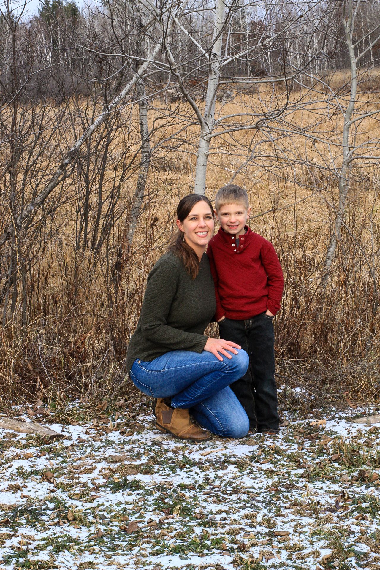 Winter outdoor portrait with snow patches and bare trees in background.