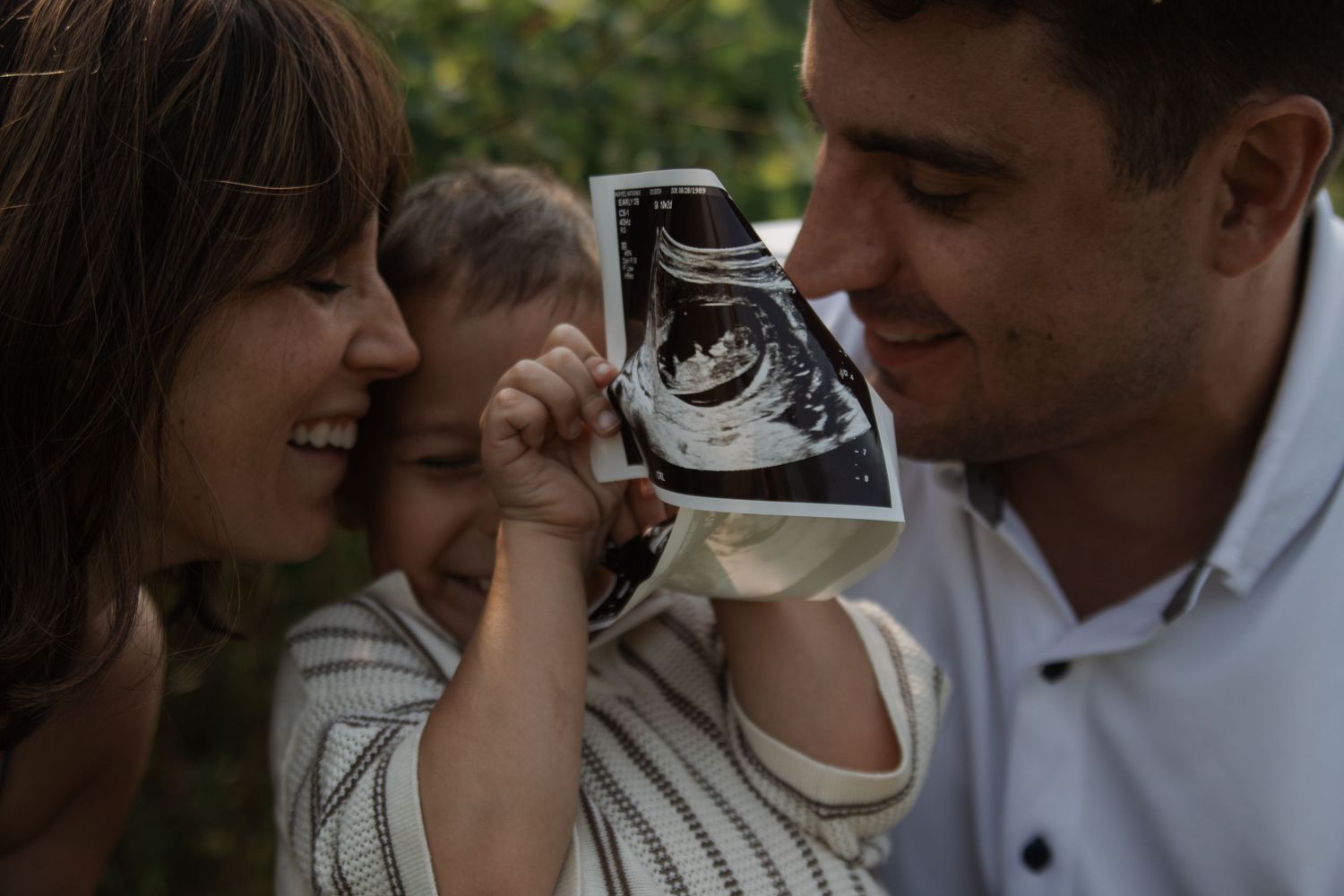 Couple sharing intimate moment while looking at ultrasound photos outdoors.