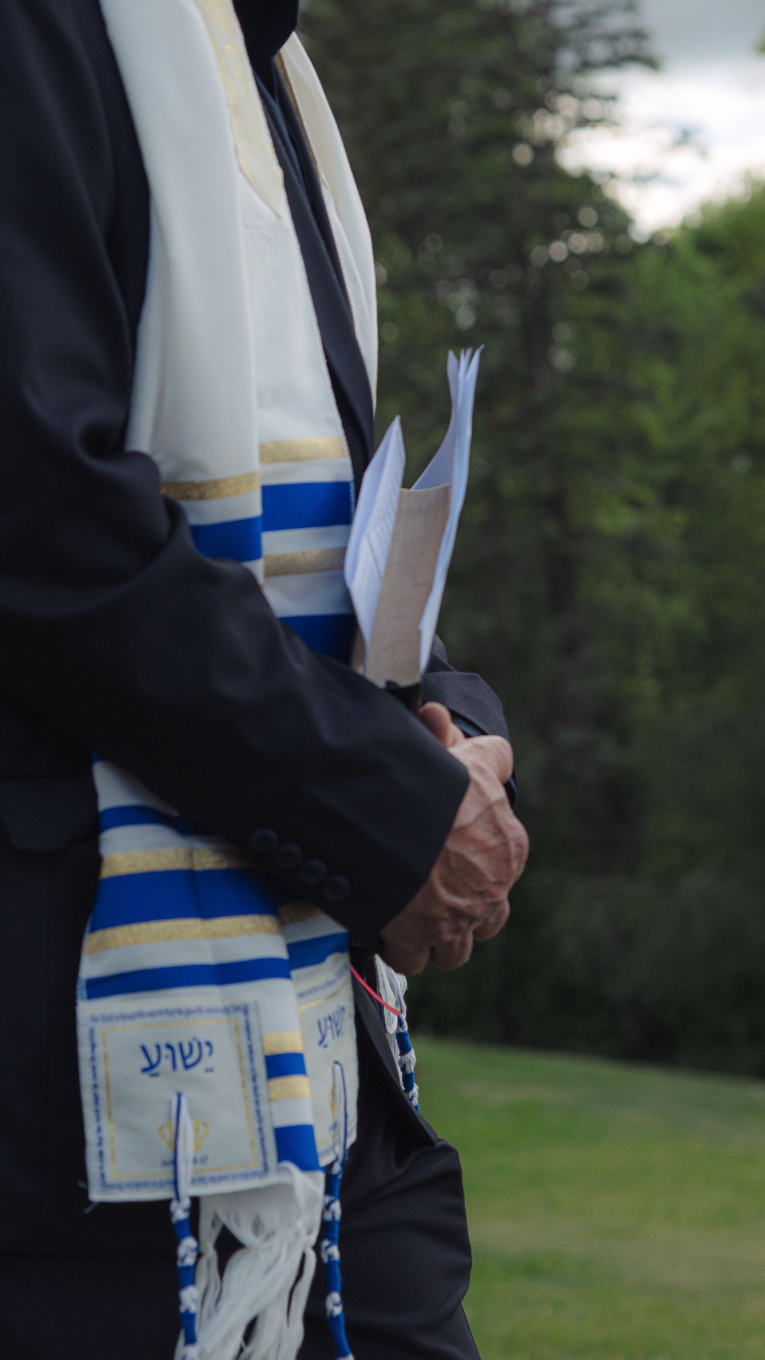 A close-up view of a tallit katan with blue and white tzitzit strings against a dark background.