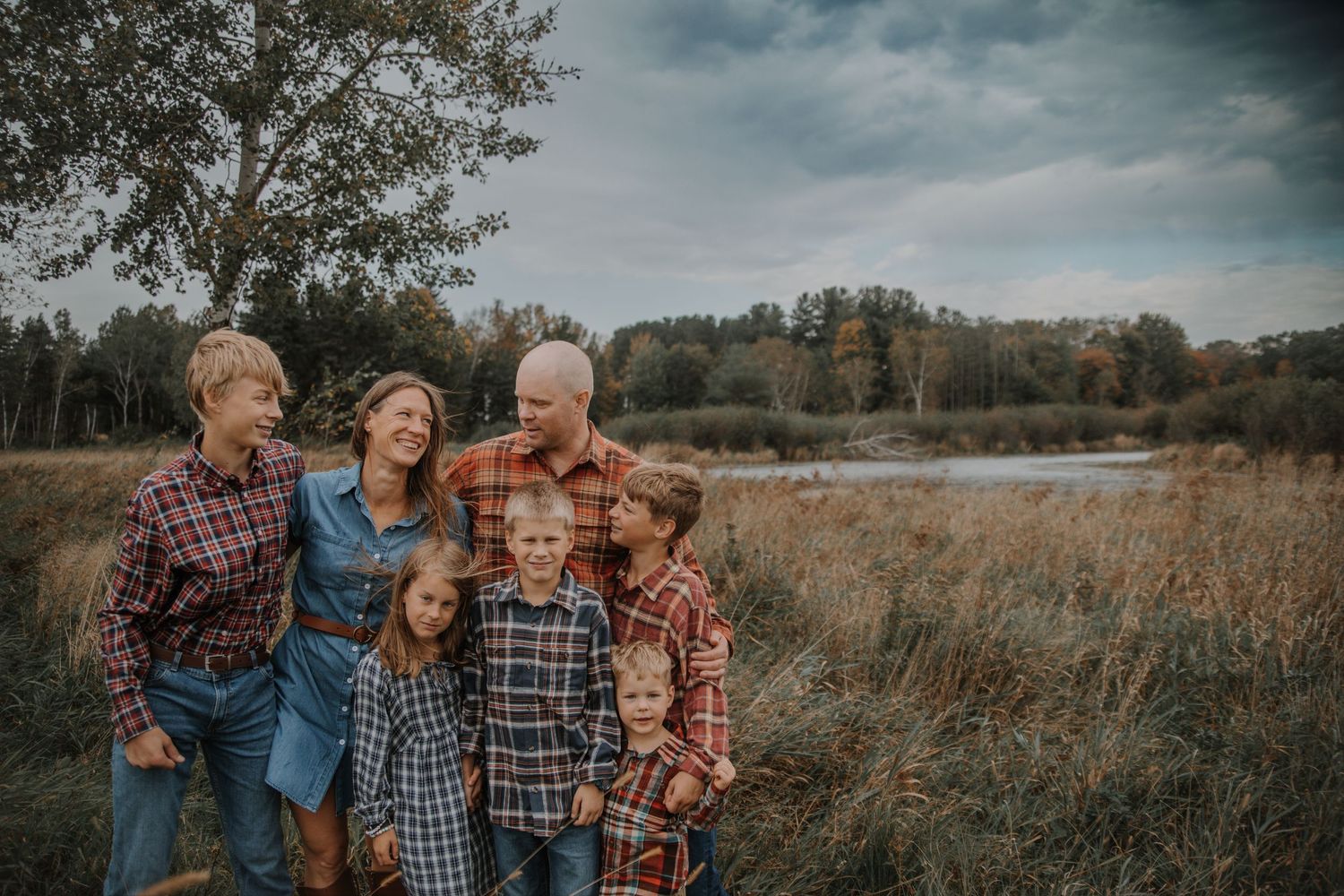 A family wearing coordinating plaid outfits shares joyful moments together in a golden autumn field at sunset.