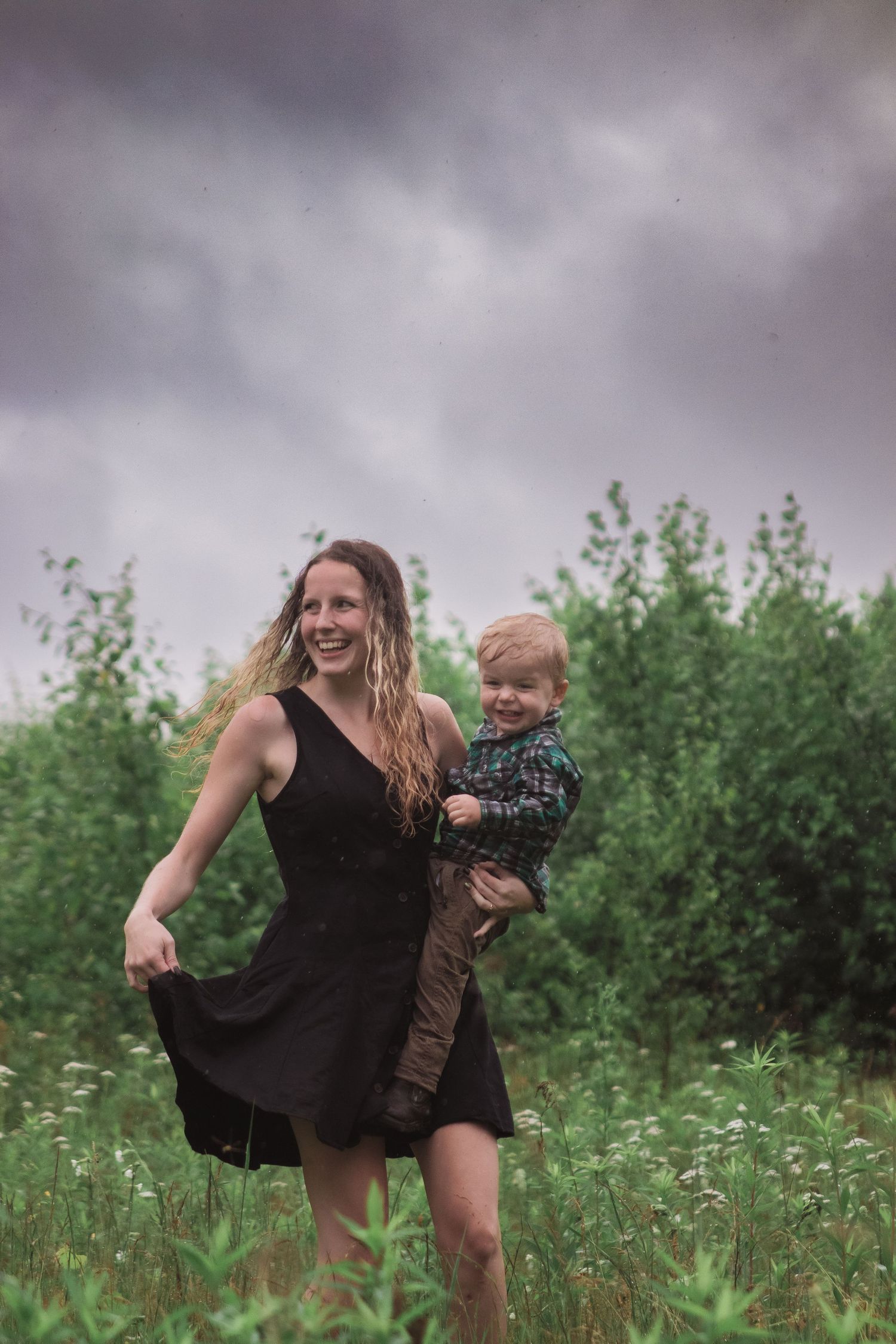 A mother and child share playful moments together in a flowering meadow beneath stormy clouds.