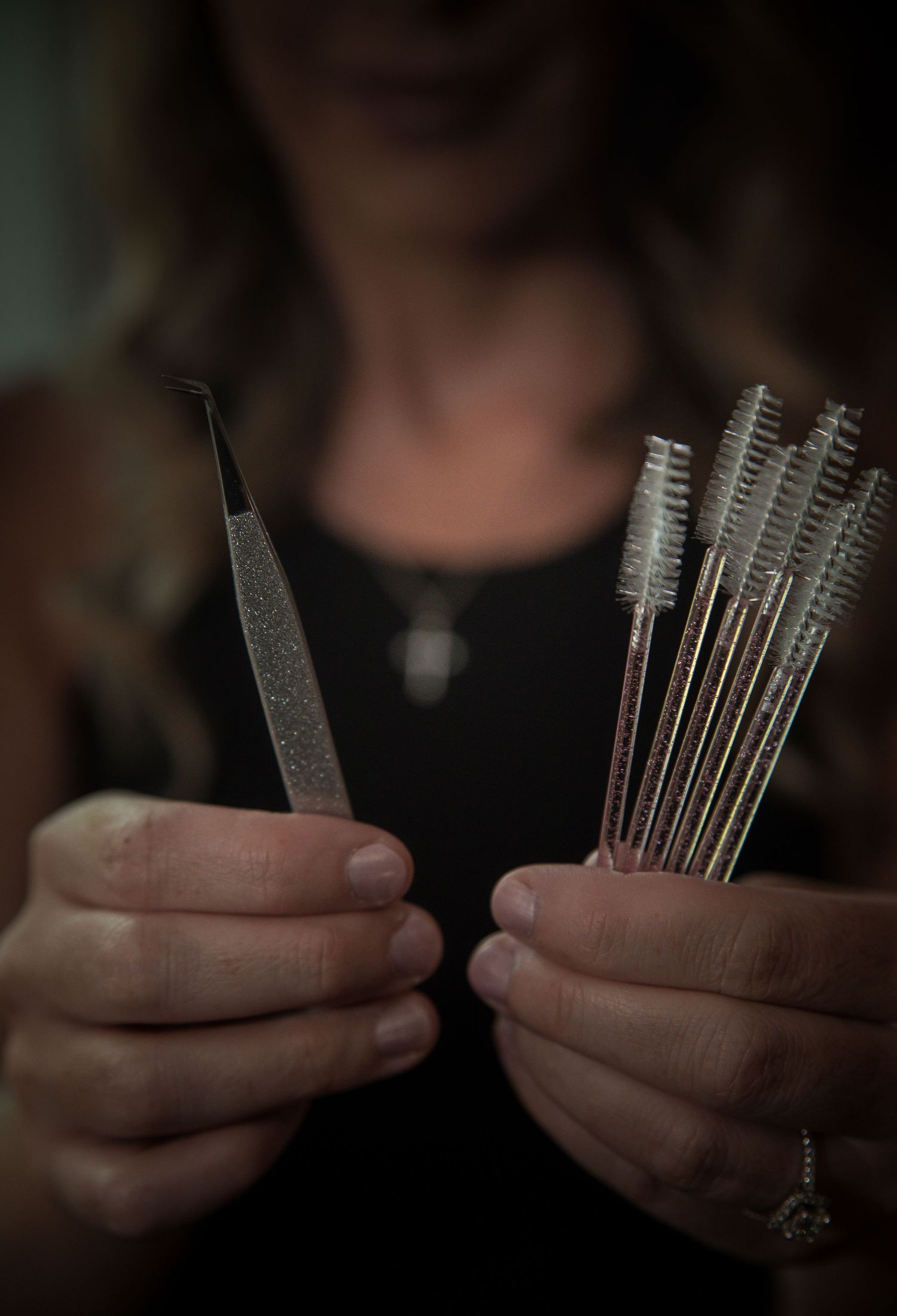 Close-up view of hands comparing tools and brushes for cosmetic or makeup application in low light conditions.