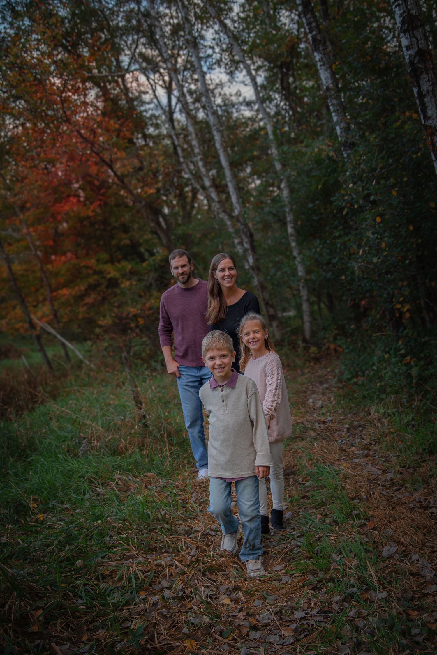 A group walks together on a leaf-covered forest path during autumn with trees showing fall colors.