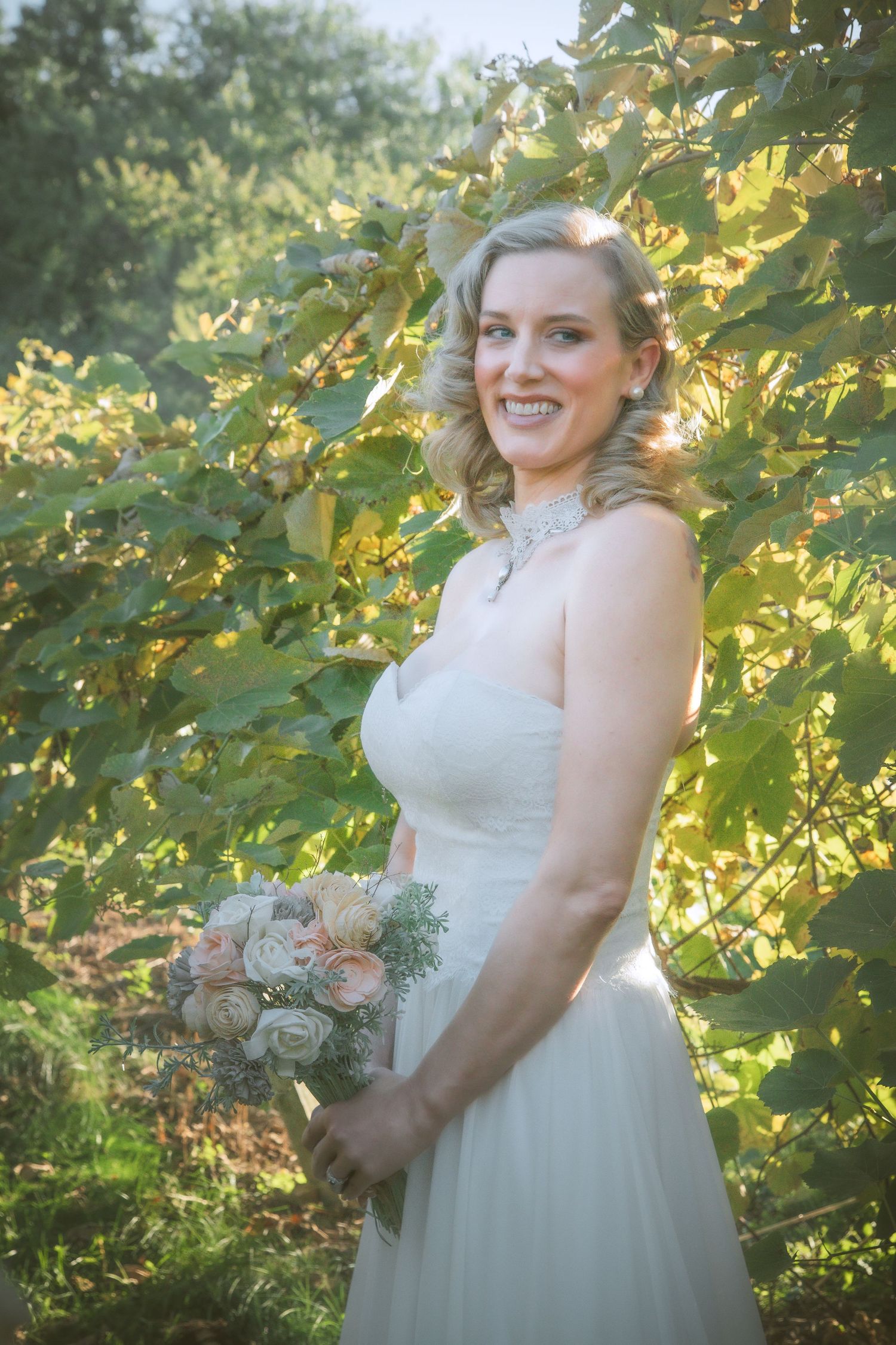 Bride in white lace gown poses outdoors against sunlit greenery with delicate bouquet in a series of portraits.