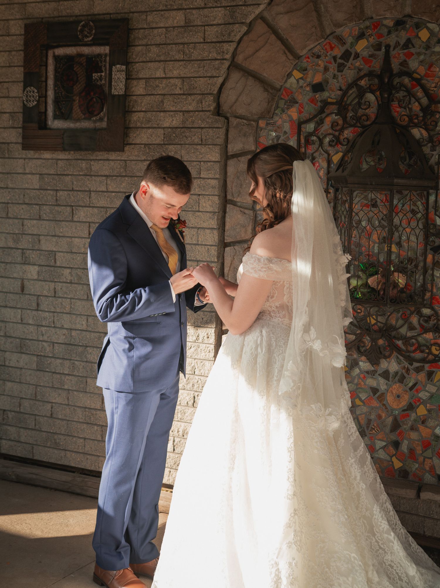 A couple exchanges rings during their wedding ceremony in front of a rustic brick wall backdrop.