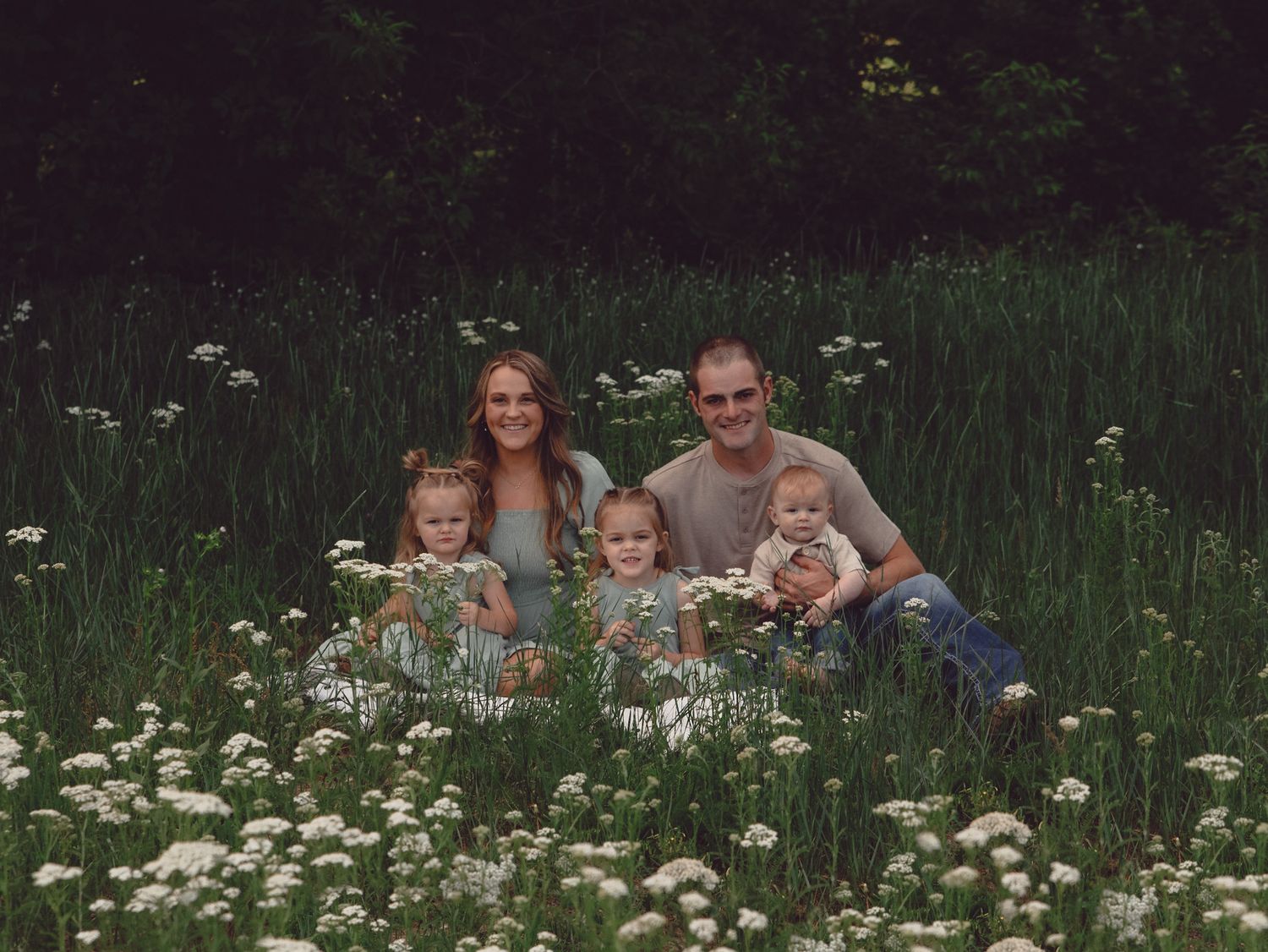Family of five posing in a wildflower meadow surrounded by lush greenery and white blooms.