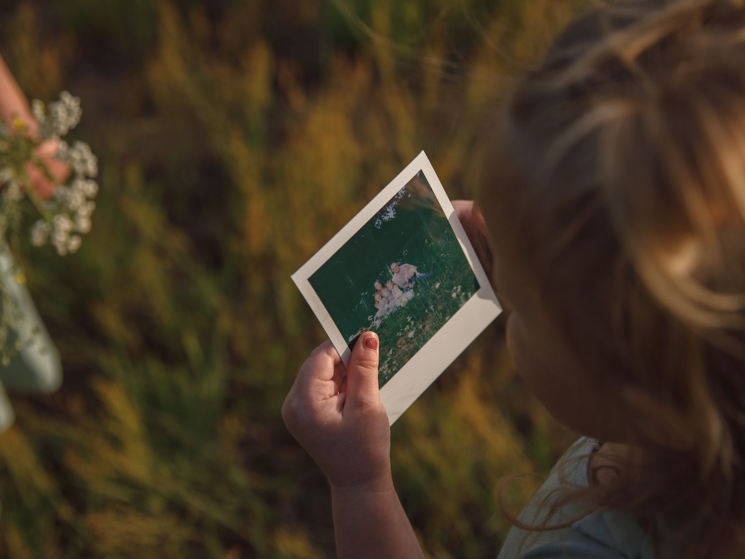 Young child holding a Polaroid photo of flowers while standing in a field.