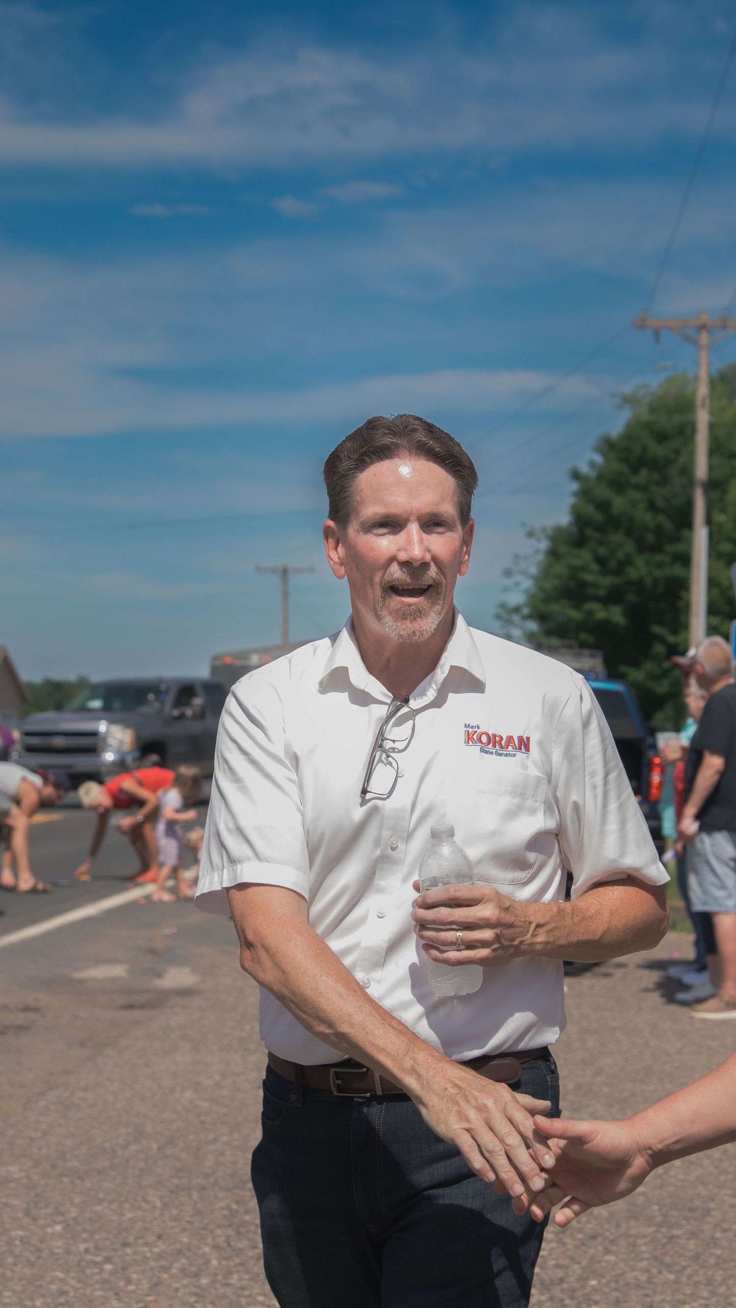 Person in white uniform greeting attendees at an outdoor community event on a sunny day.