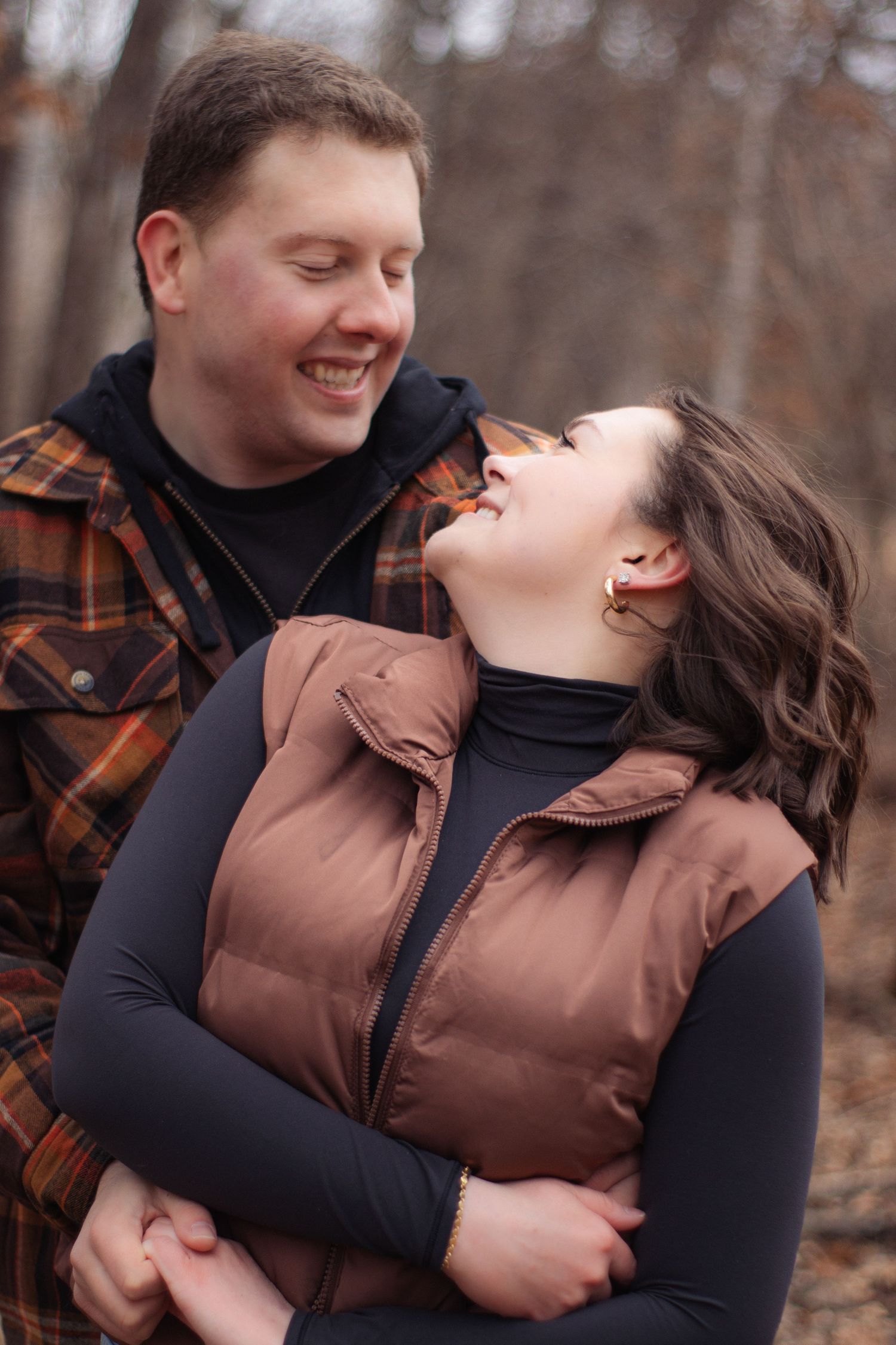 A joyful couple sharing a laugh together while wearing winter coats in an autumn forest setting.