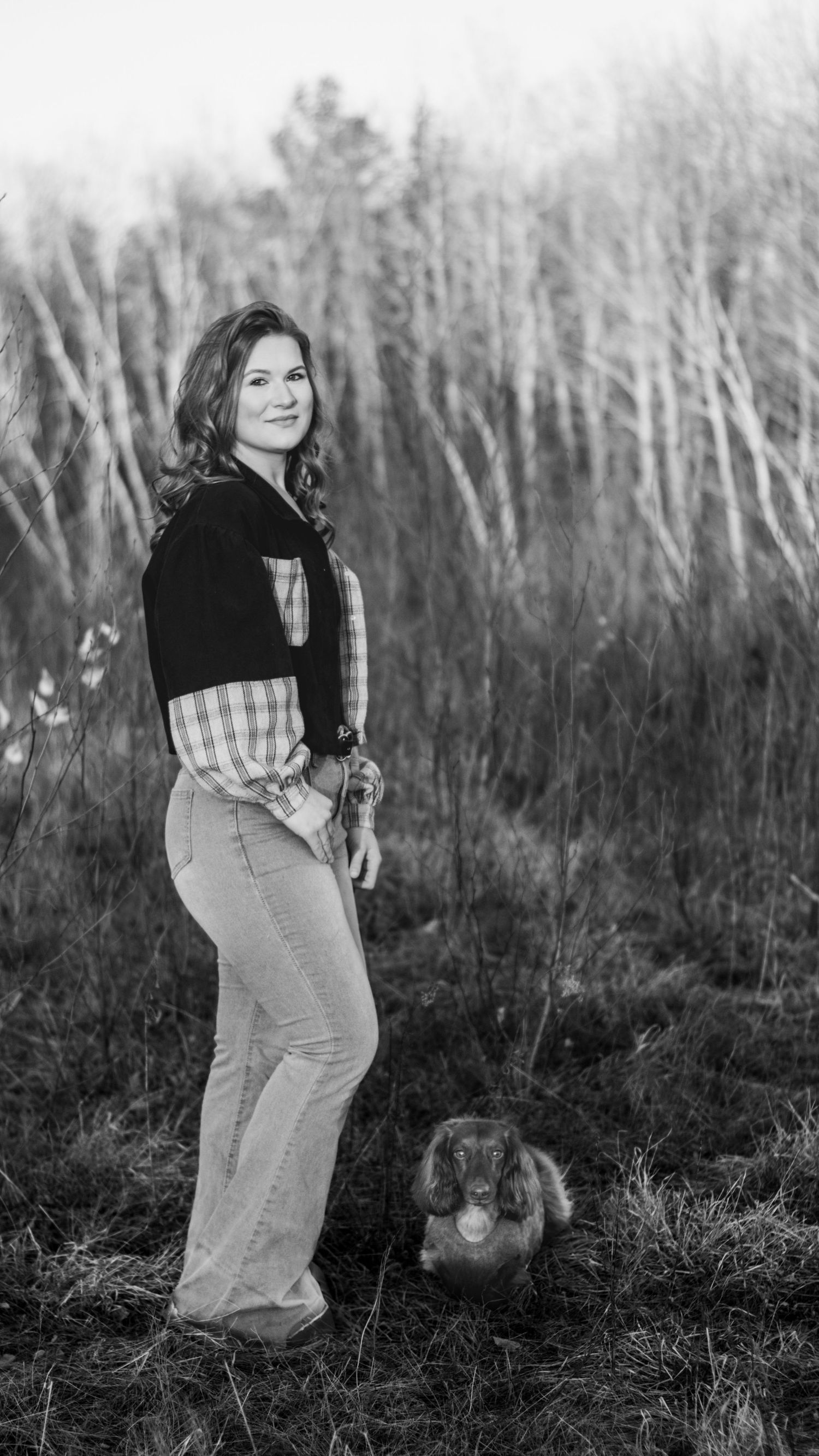 Smiling woman in flare jeans posing with a rabbit in a field in black and white.